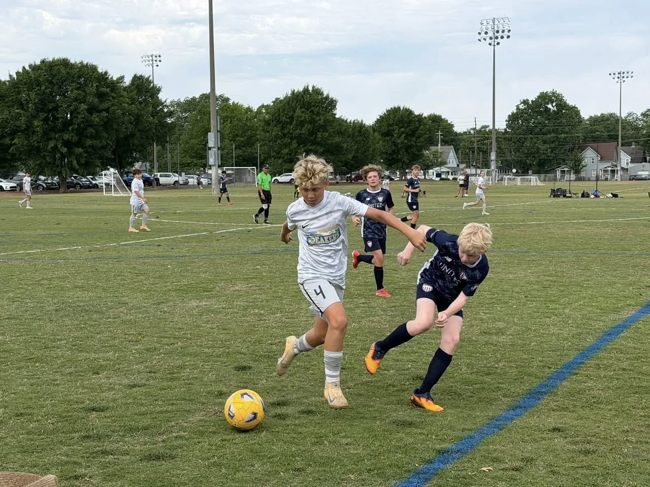 Two young boys playing soccer, contesting for the ball on a field during a youth soccer game, surrounded by other players and coaches.