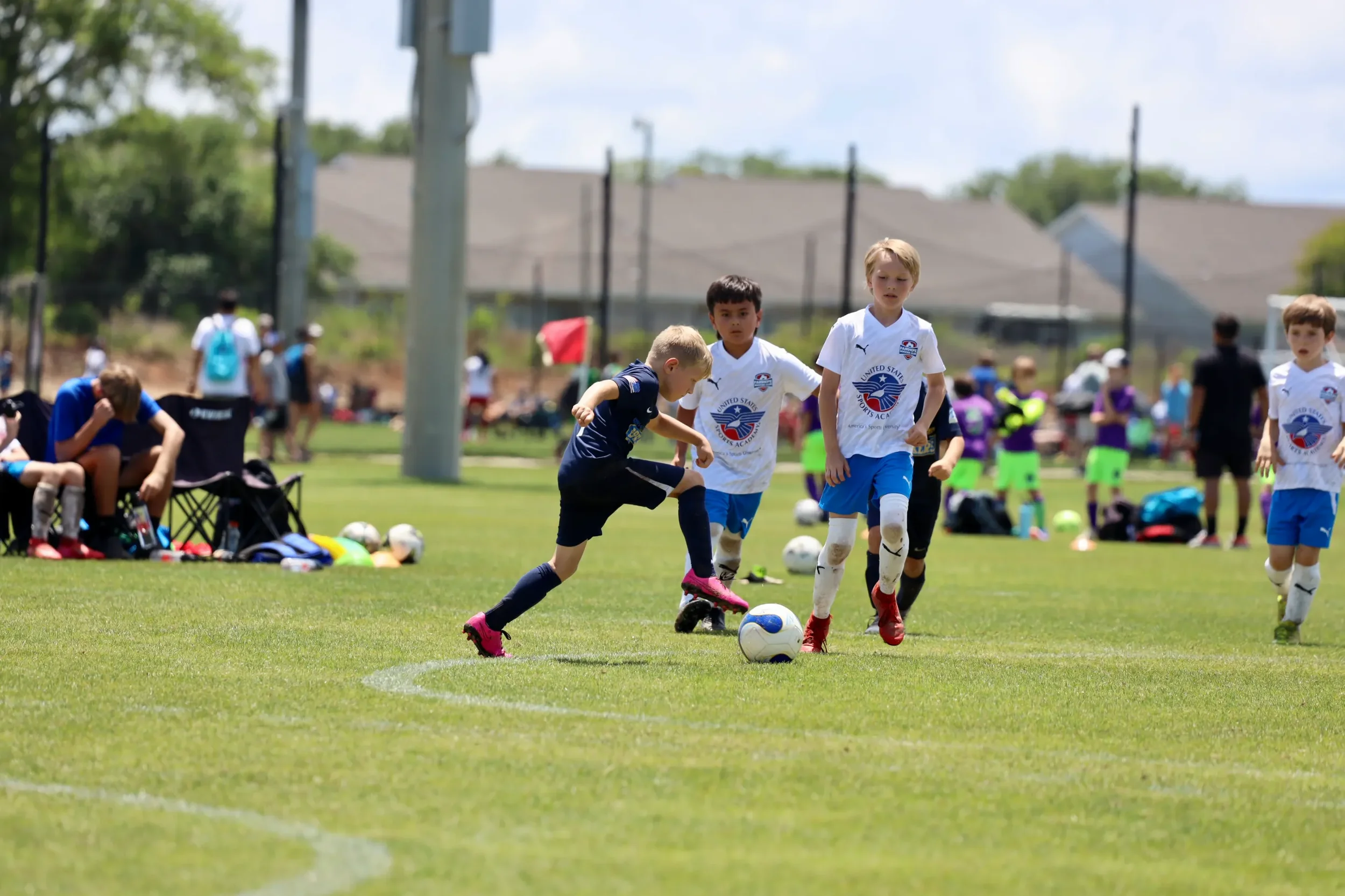 Young boys playing soccer on a field during daytime, surrounded by spectators and coaches.