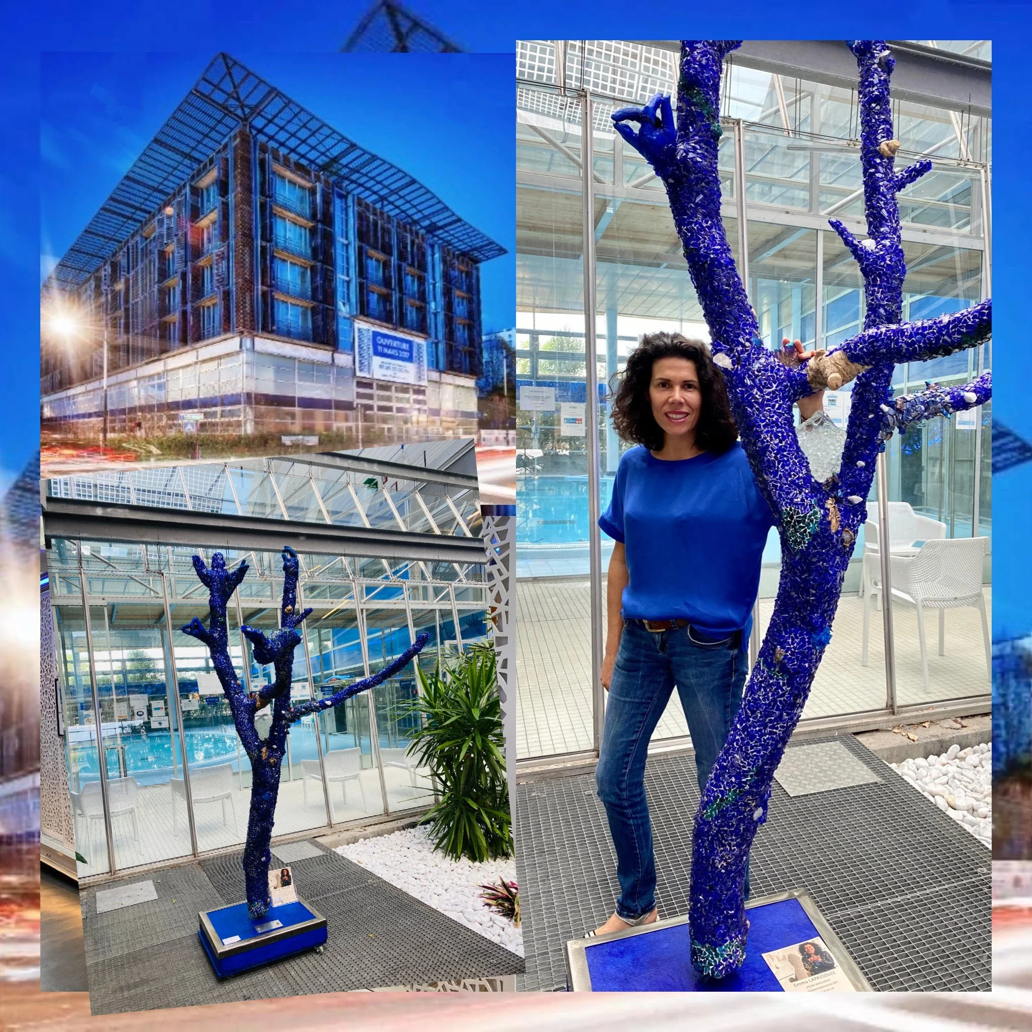 Une sculpture d'arbre bleu en mosaïque dans un centre commercial, avec une femme posant à côté. La sculpture est faite de morceaux de verre et a des branches bleues.