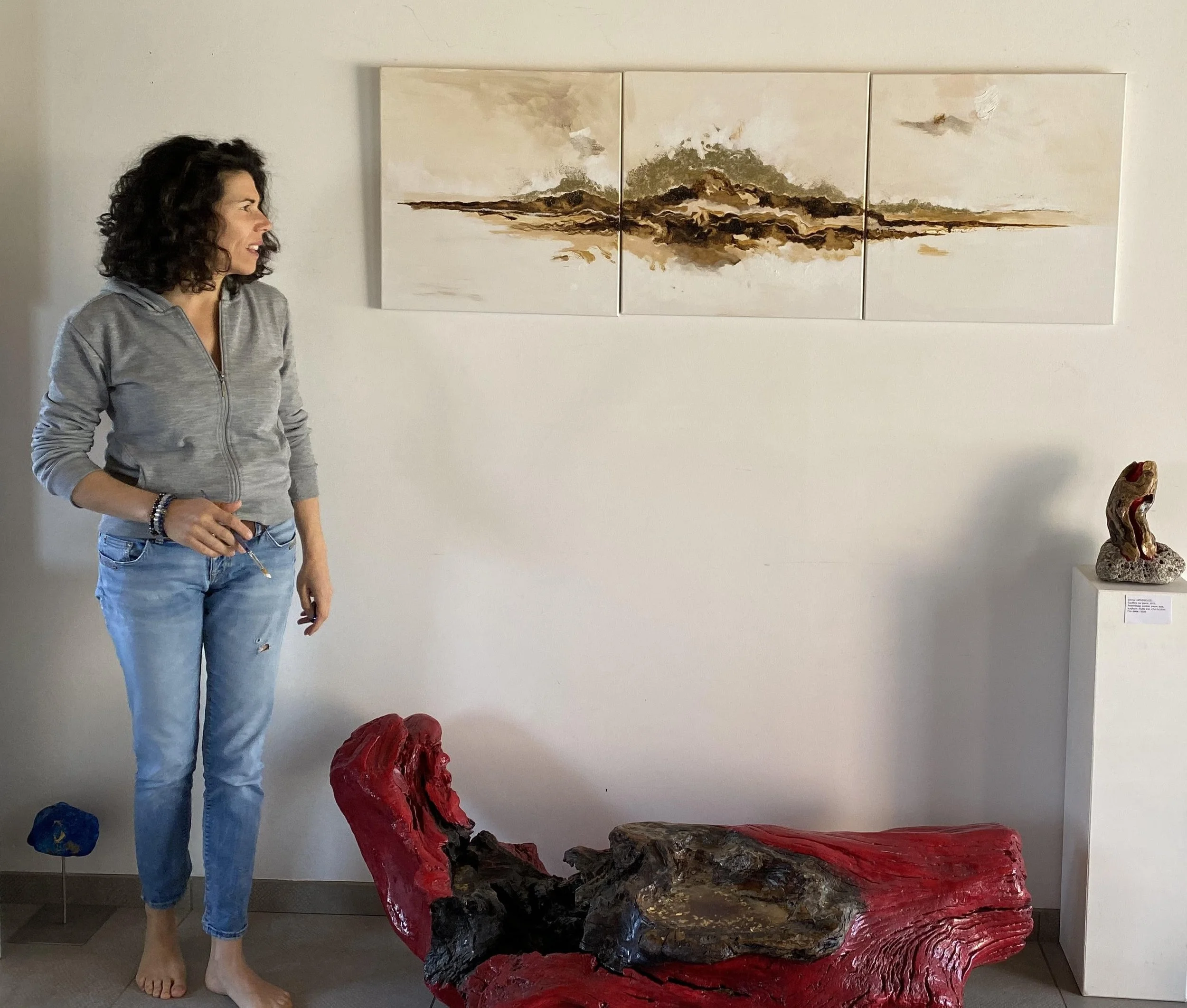 Une femme debout à côté d'œuvres d'art modernes dans une galerie.   Des sculptures colorées et une peinture abstraite en triptyque sont visibles dans l'image.