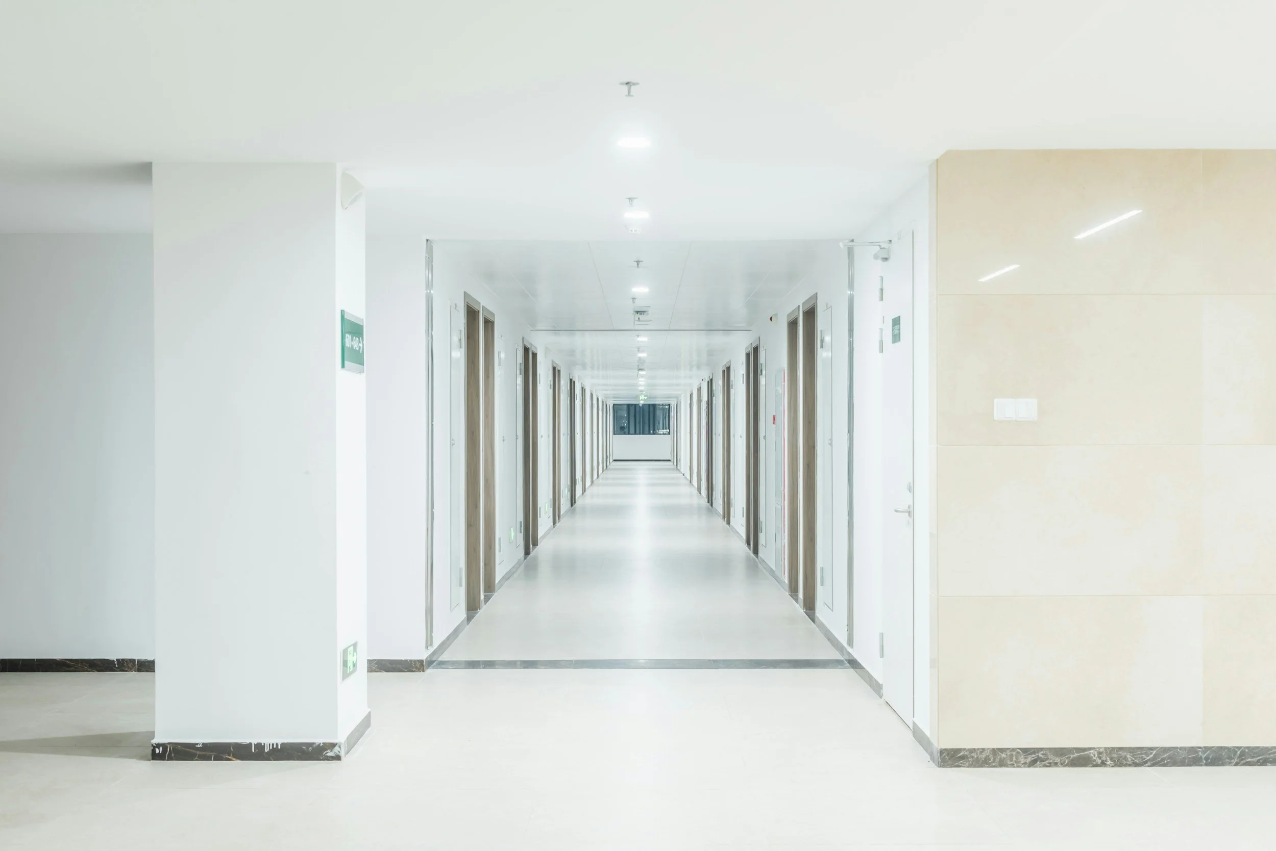 Empty corridor in a modern remodeled hospital building with multiple elevator doors and ceiling lights. Hospital electrical services provided in central Oregon and Oregon coast.