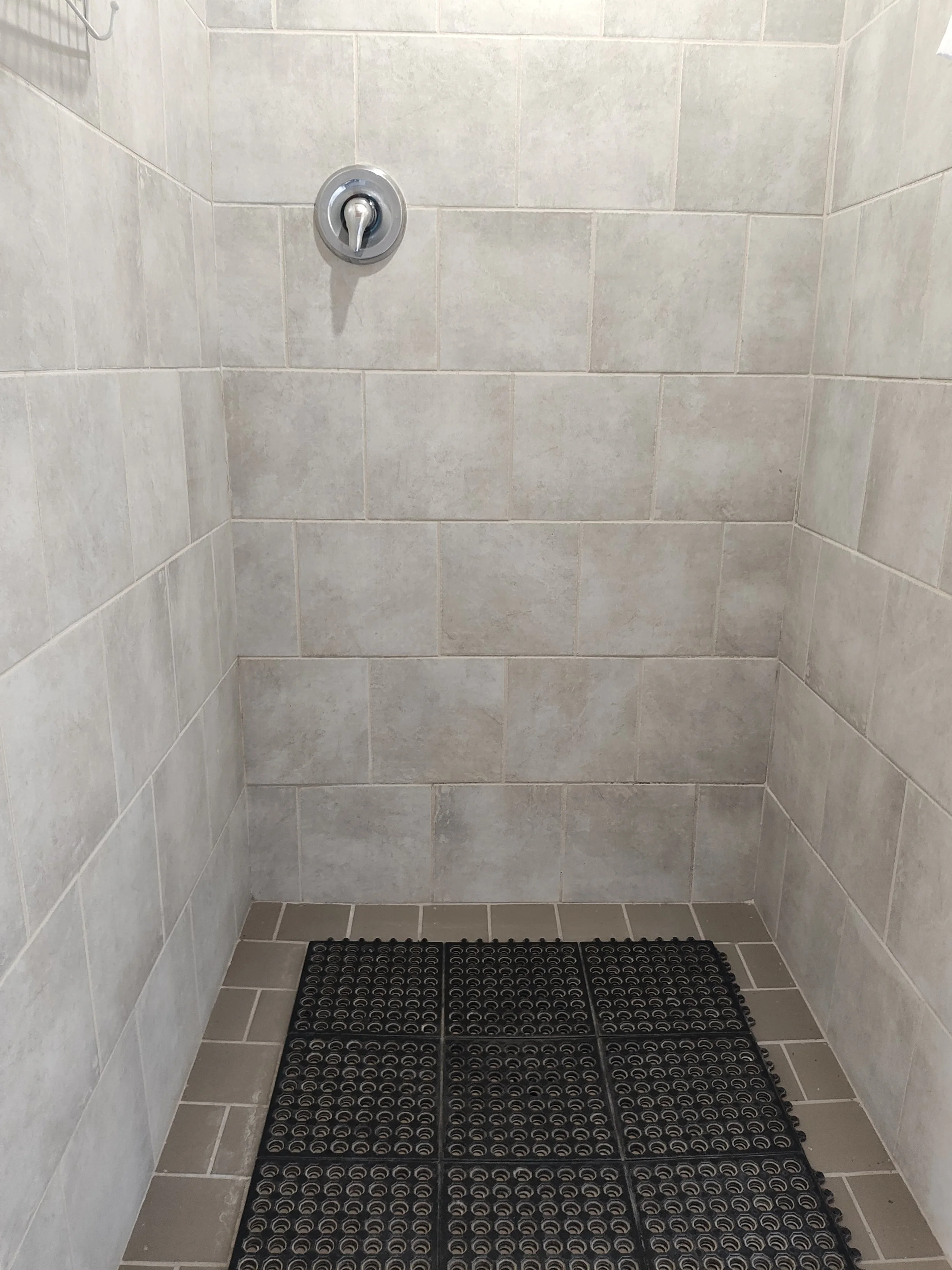 Shower stall with beige tiled walls and floor, black rubber shower mat at the bottom.