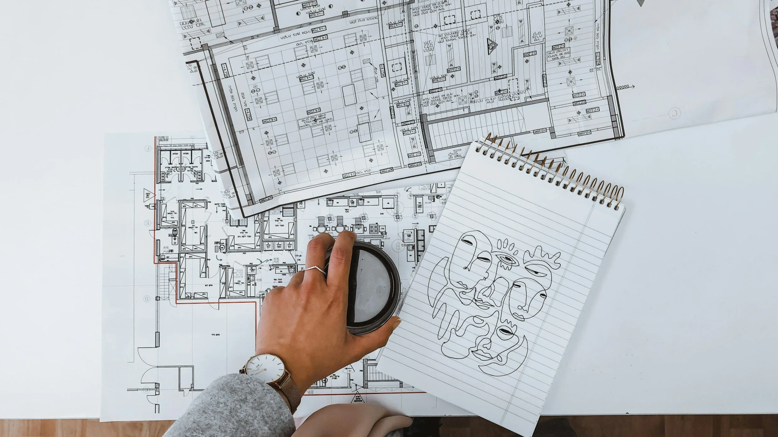 Person's designing over architectural blueprints, with notebooks, drawings, and planning documents.
