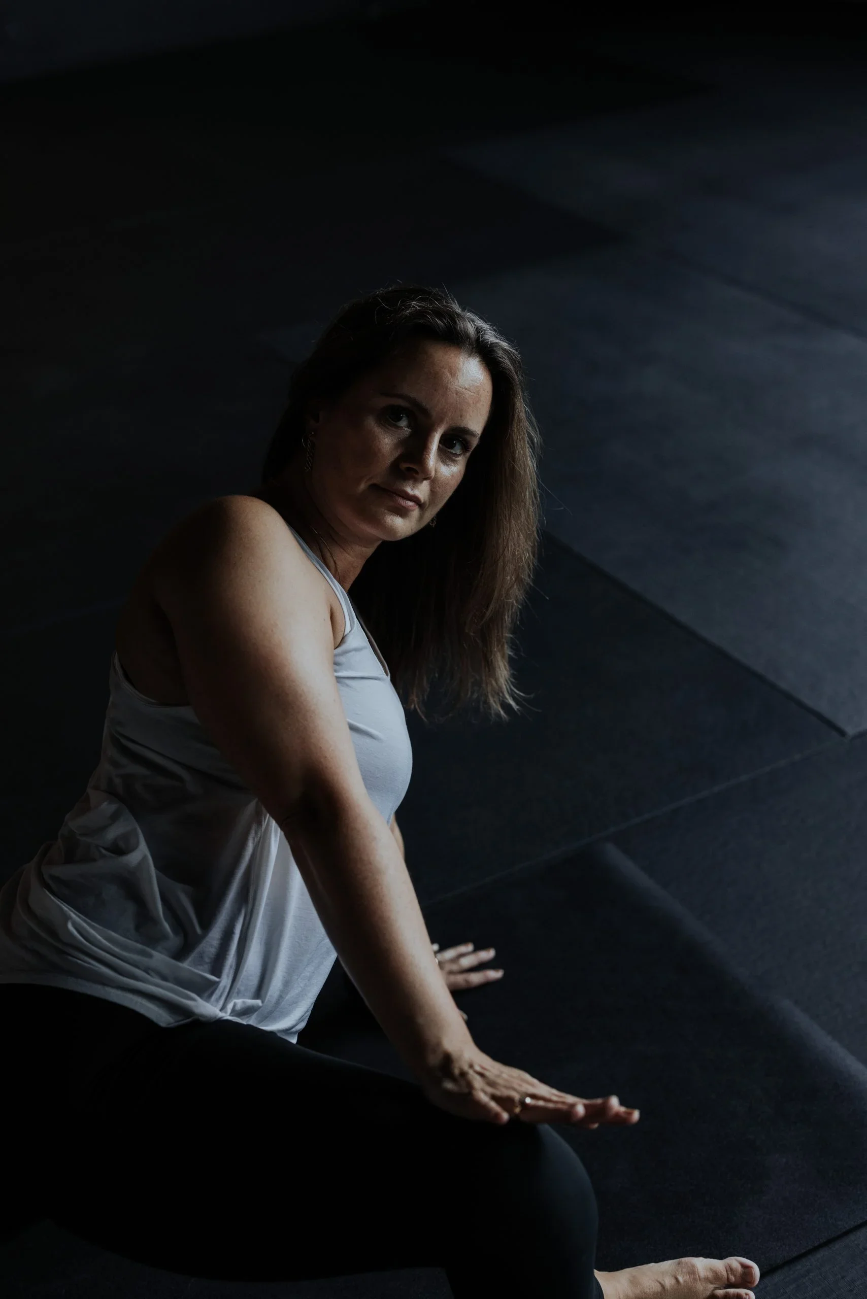 A woman practicing yoga on a dark floor, dressed in athletic wear, in a dimly lit room.
