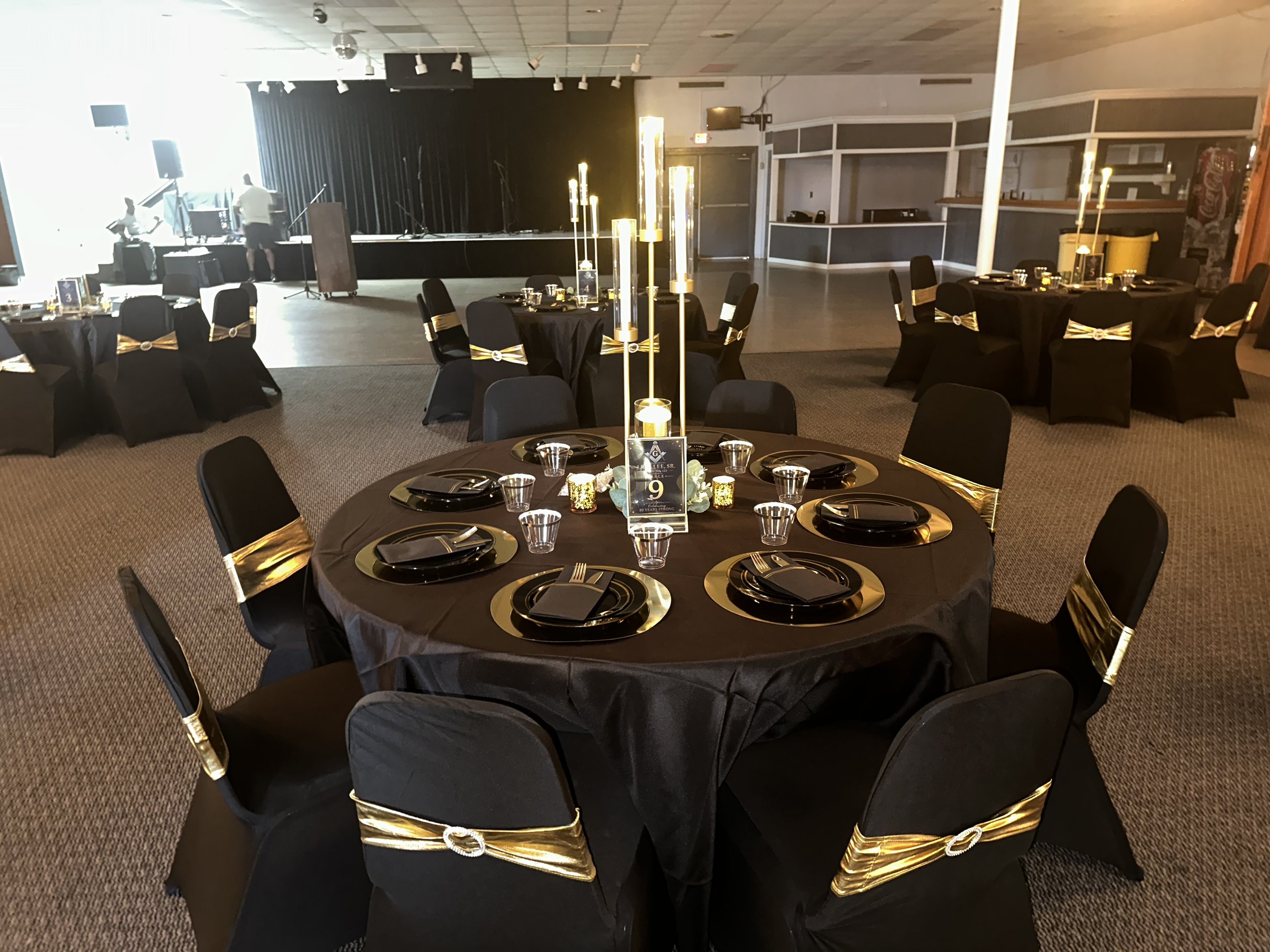 Event hall decorated for a formal celebration with black tablecloths, gold accents, and candelabra centerpieces, designed by MPR Events LLC.