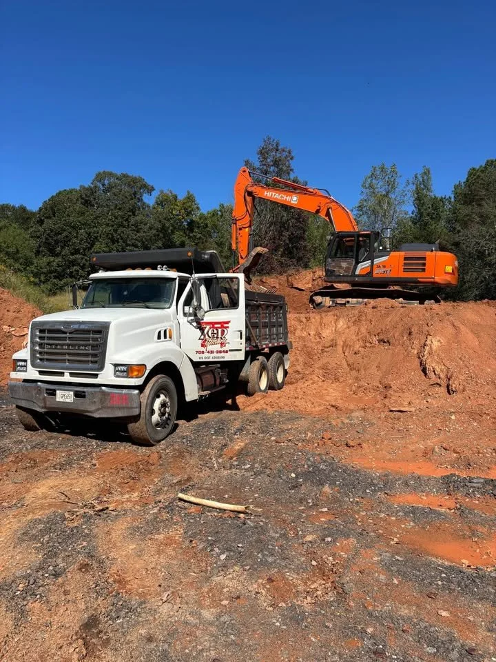 Heavy excavator loading a dump truck for dirt export and site hauling services in Northeast Georgia by Taproot Contracting.