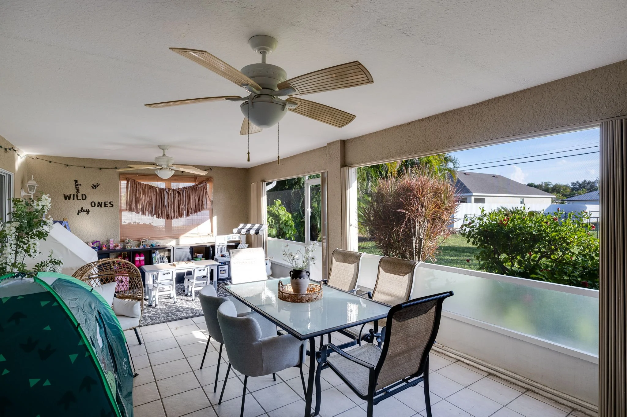 Sunroom with ceiling fans, large windows, and outdoor view of trees and neighboring houses.