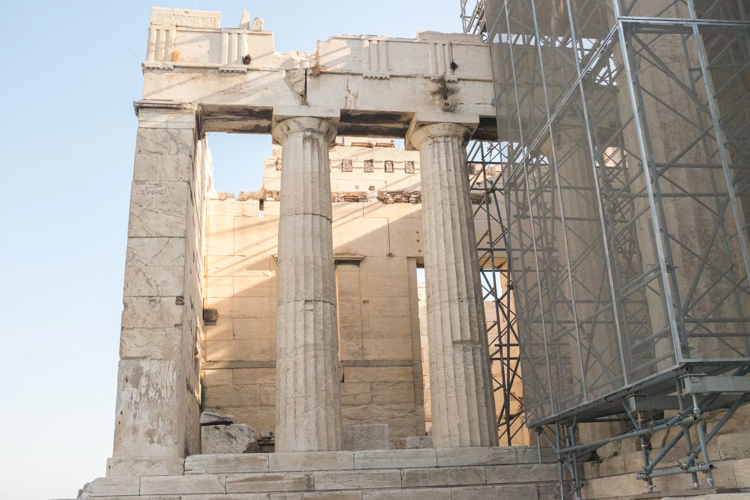 Ancient Greek ruins of columns and stone structure partially covered by scaffolding on the right side.