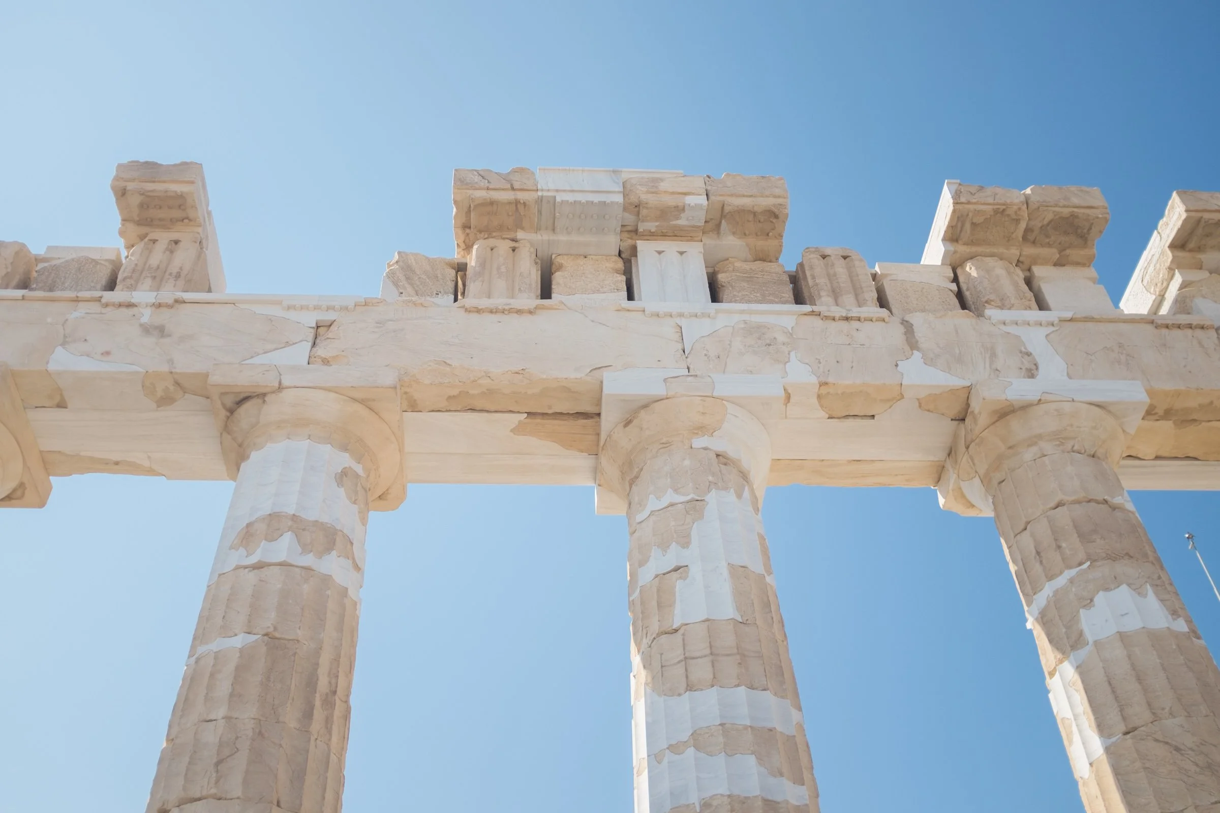 Ancient Greek ruins with tall marble columns and architectural fragments under a clear blue sky.