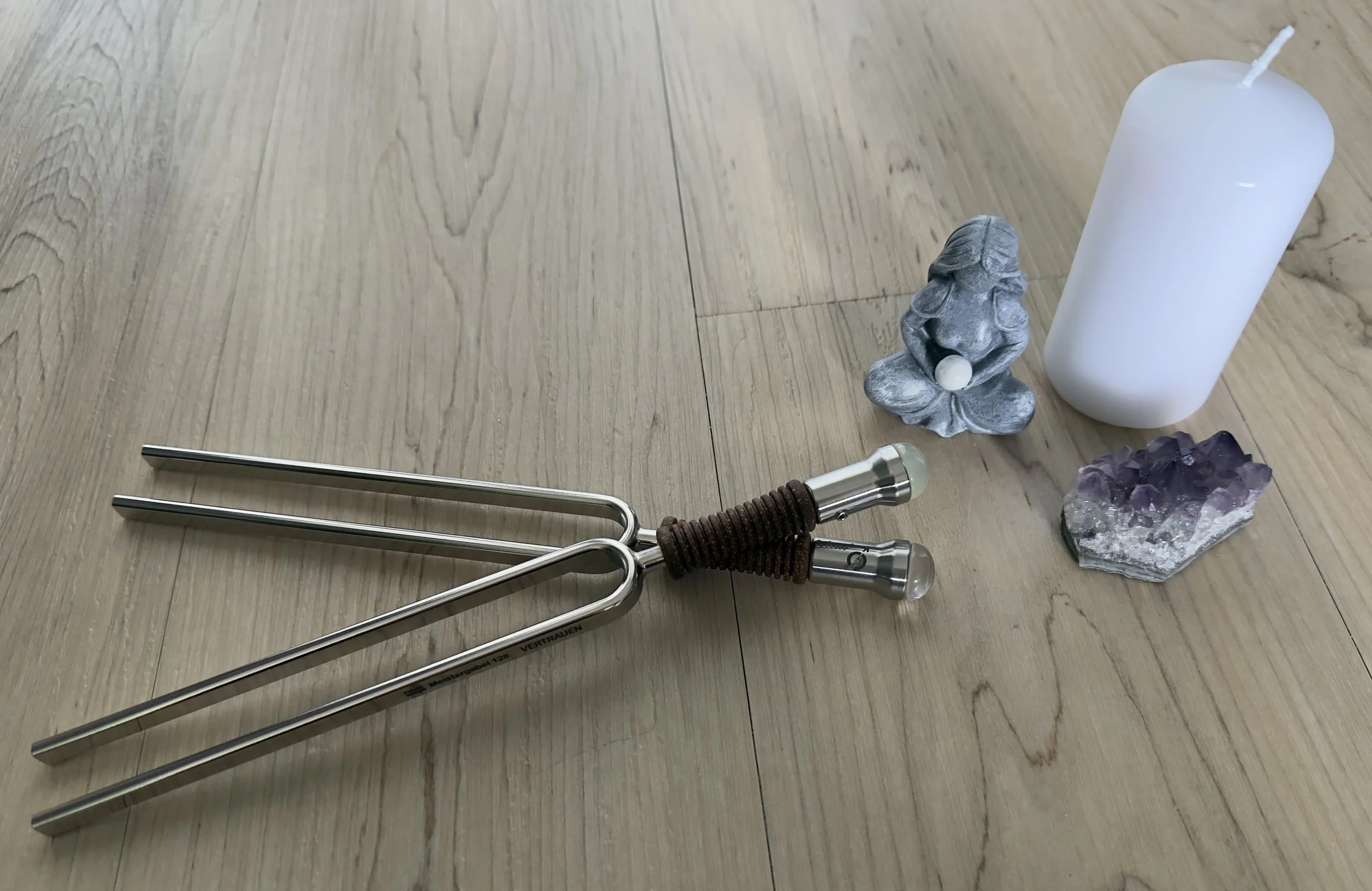 Eine weiße Kerze, eine Figur aus grauem Achat und eine Amethyst-Quartz-Kristall auf einem Holztisch.
