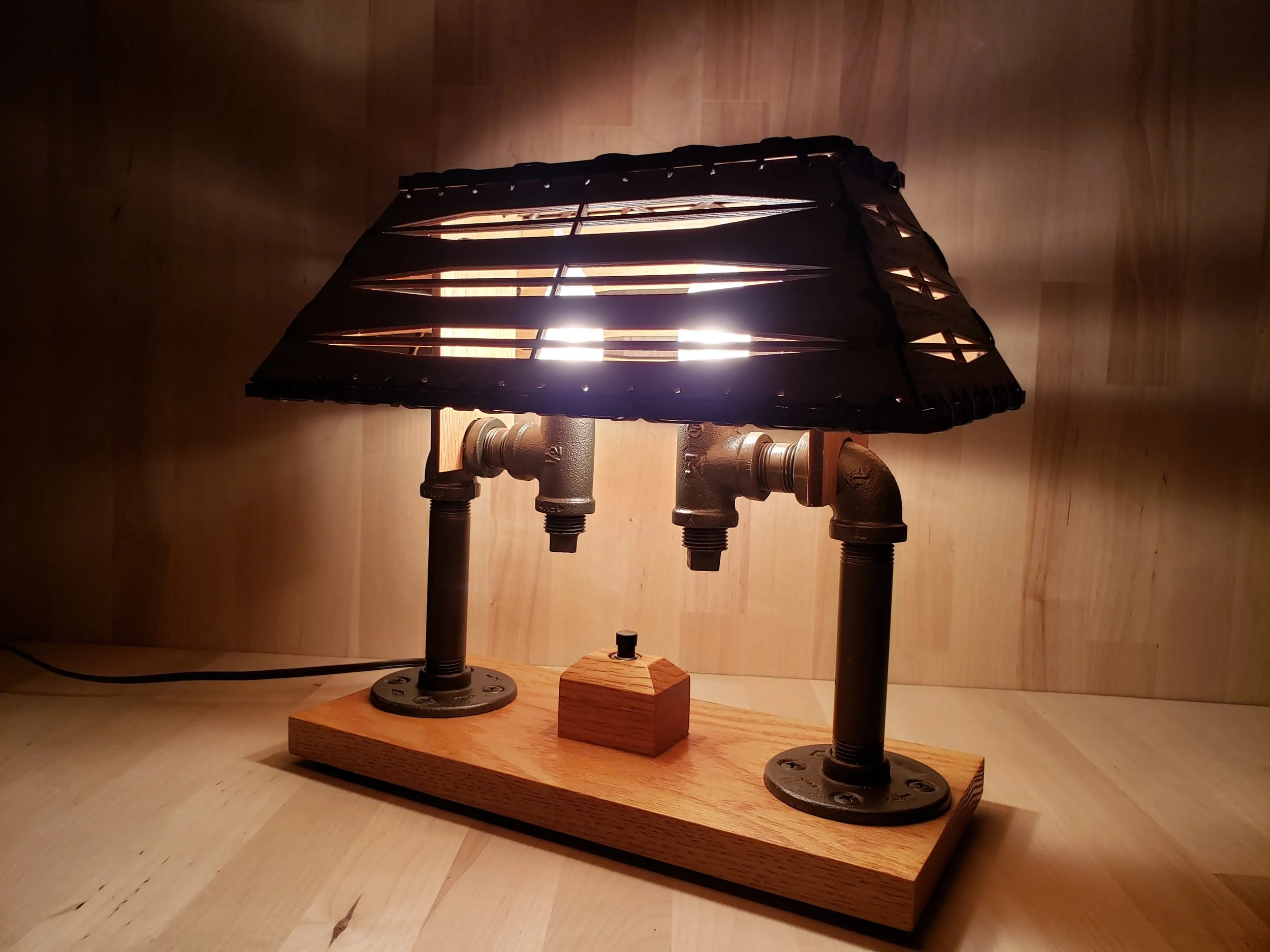 A decorative table lamp with a wooden base and a-black, basket-style lampshade, mounted on a wooden surface with a wooden background.