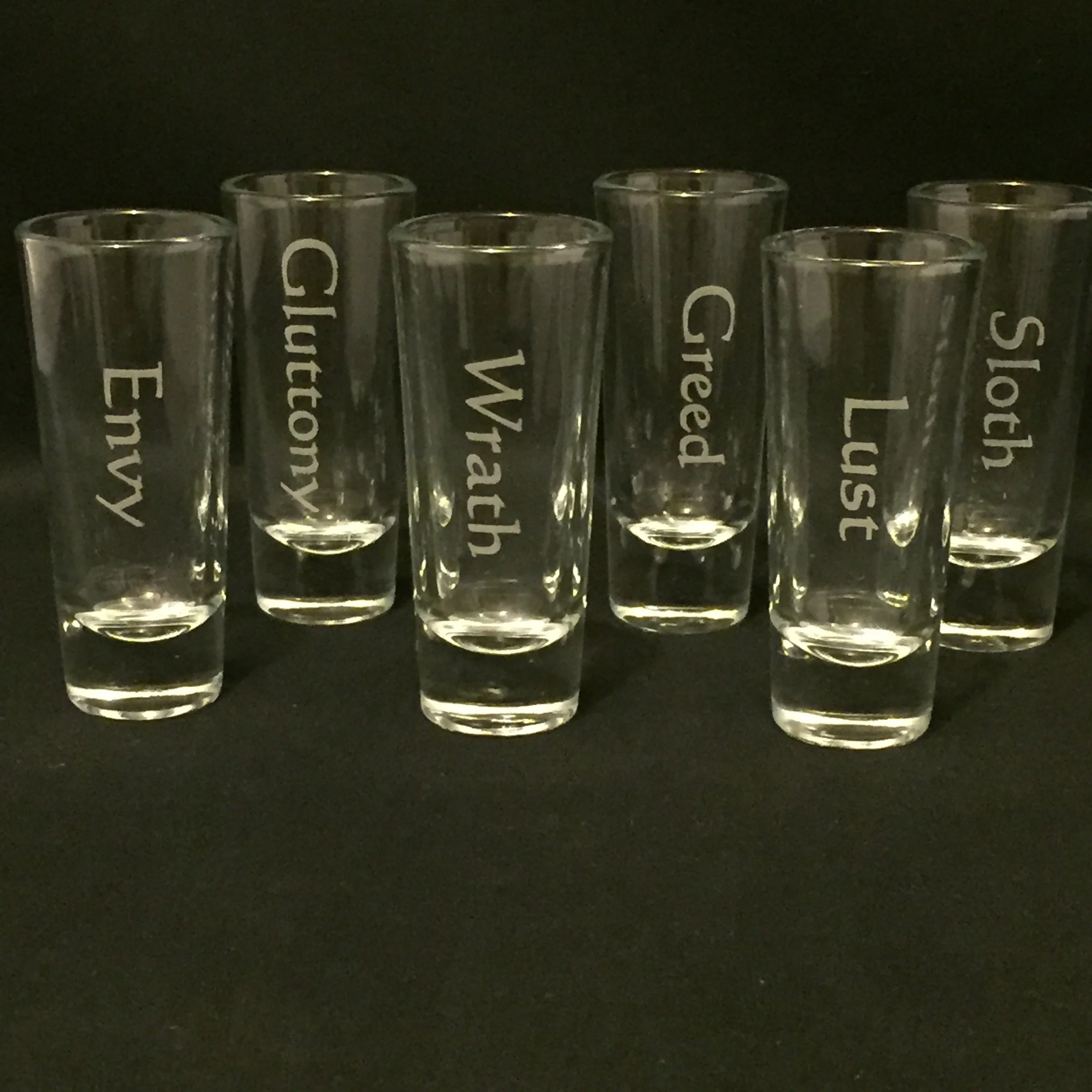 A row of seven clear glass test tubes with white text printed on them, standing upright against a black background.