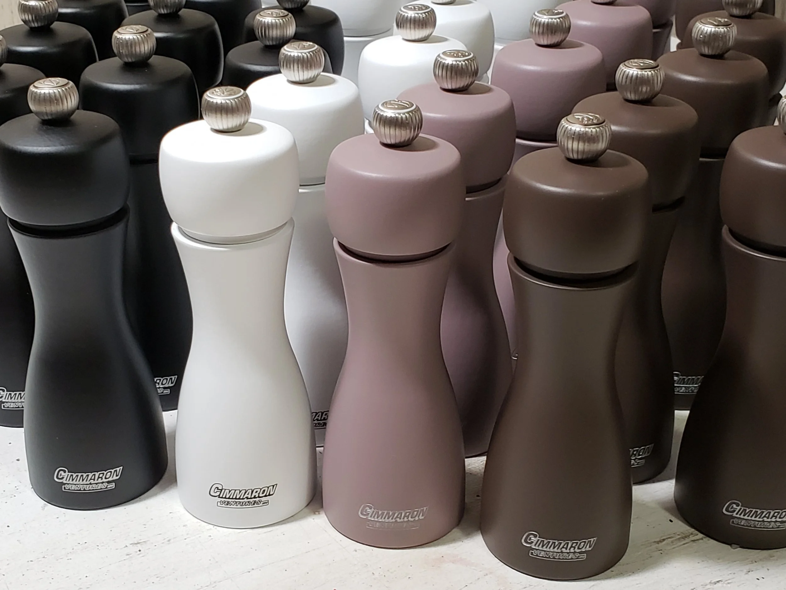 A display of various colored hydration bottles, including black, white, light pink, and dark brown, arranged in rows on a store shelf. Each bottle has a silver, ribbed screw-on lid with a logo on top.