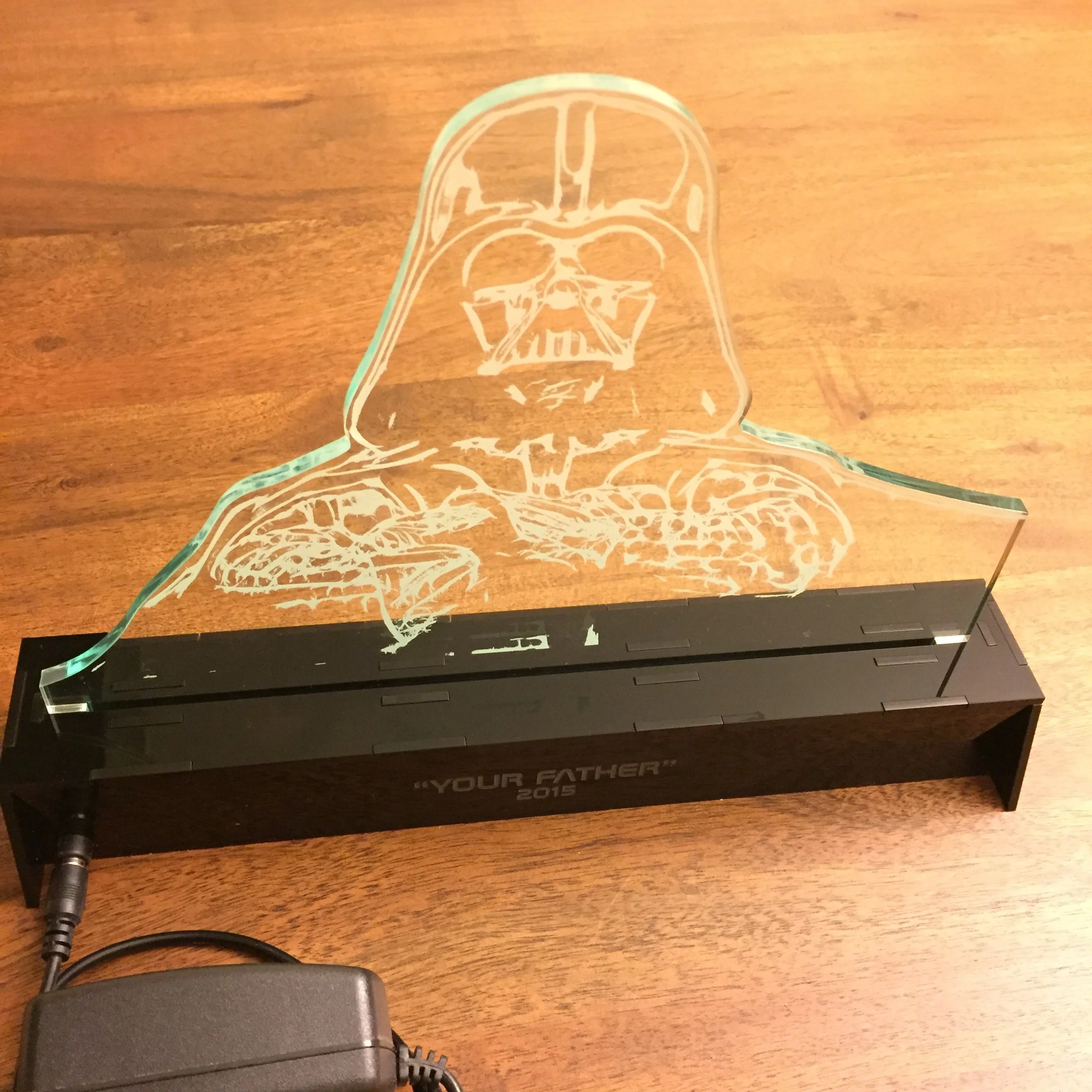 A glass decoration featuring an outline of Darth Vader's helmet from Star Wars on a wooden surface.