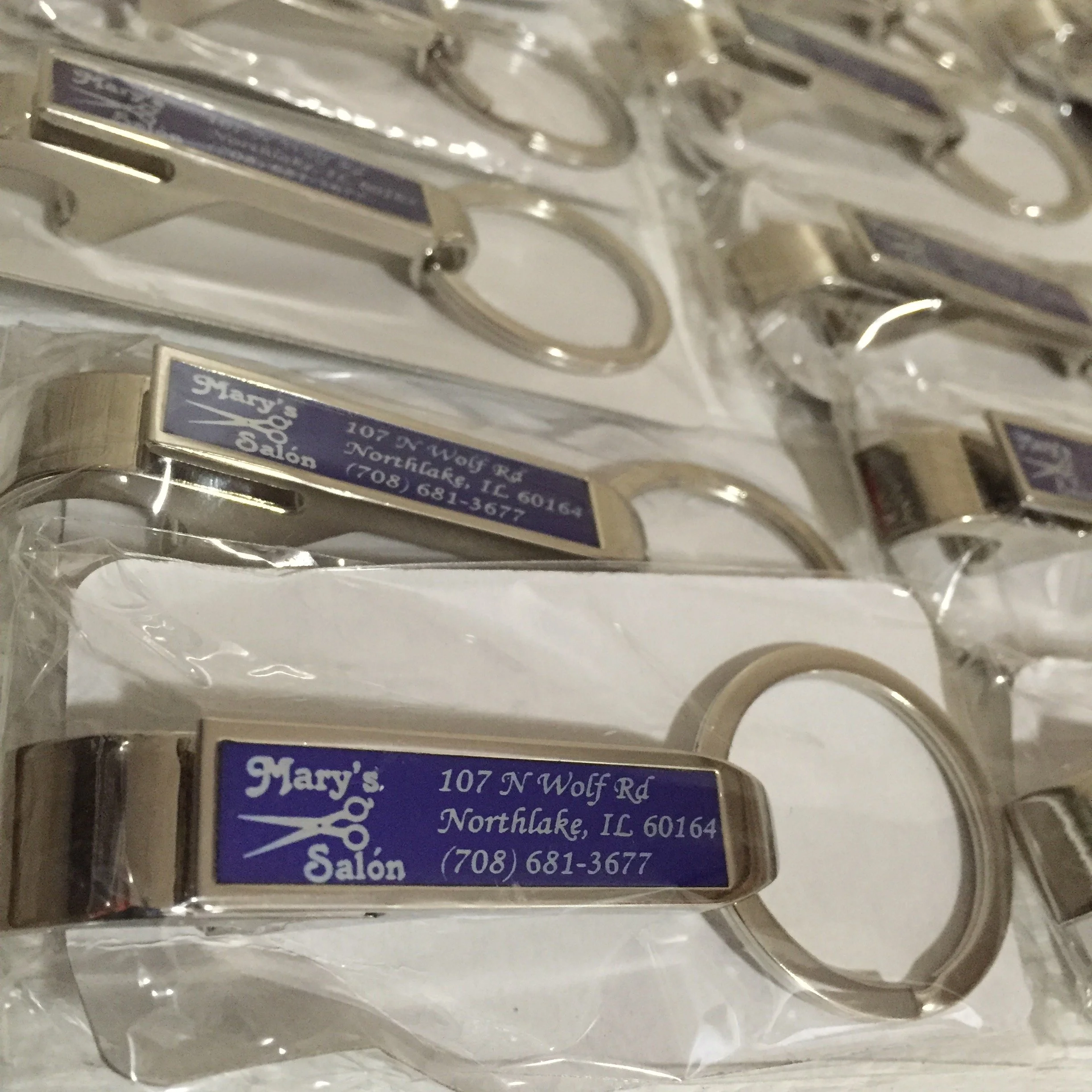 Close-up of several metal keychains with a business card attached, featuring the name, address, and phone number of a salon in Northlake, Illinois.