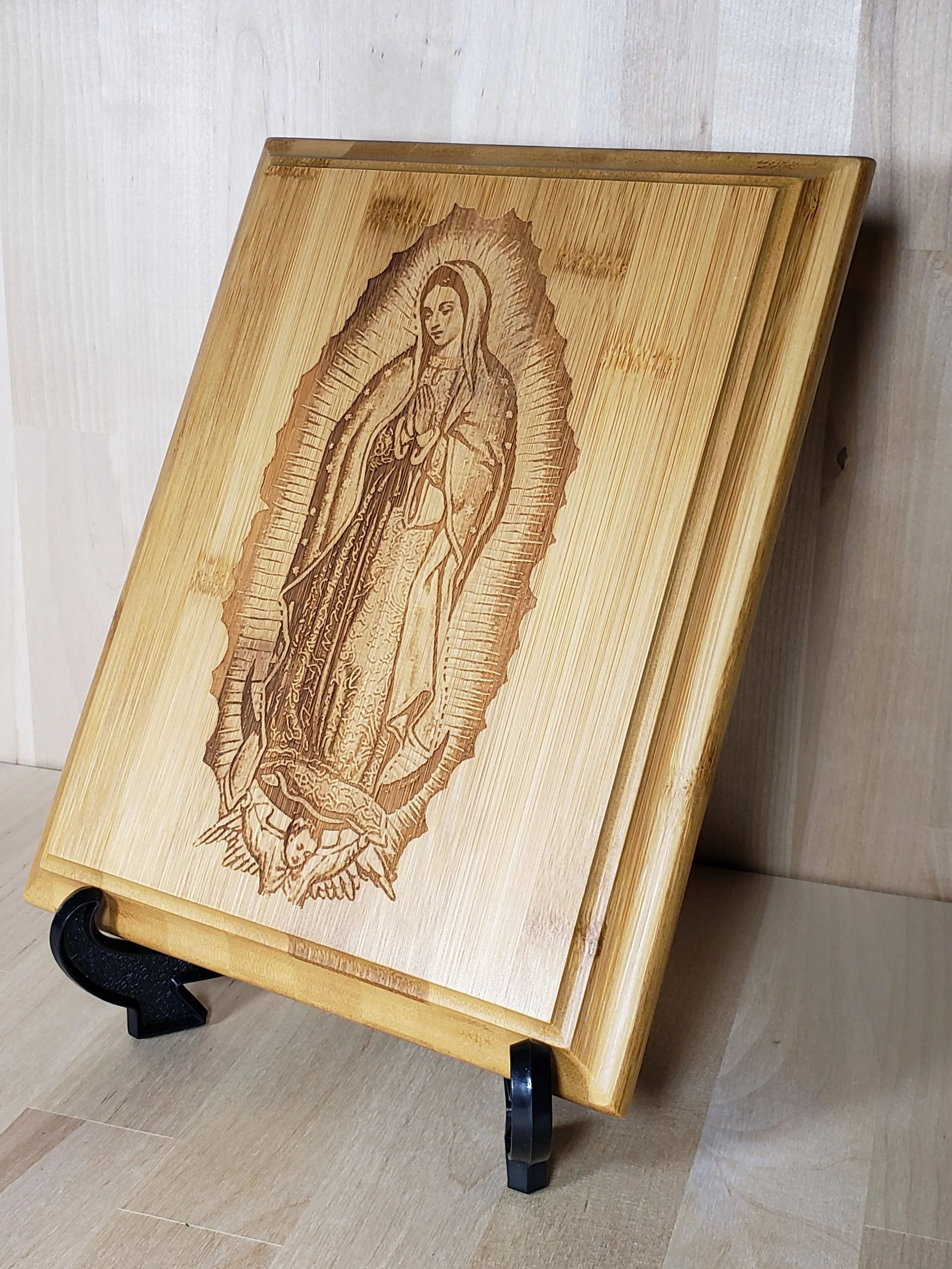 Wooden framed religious icon on a small wooden easel, depicting Our Lady of Guadalupe with a radiant halo, hands in prayer, and intricate details.