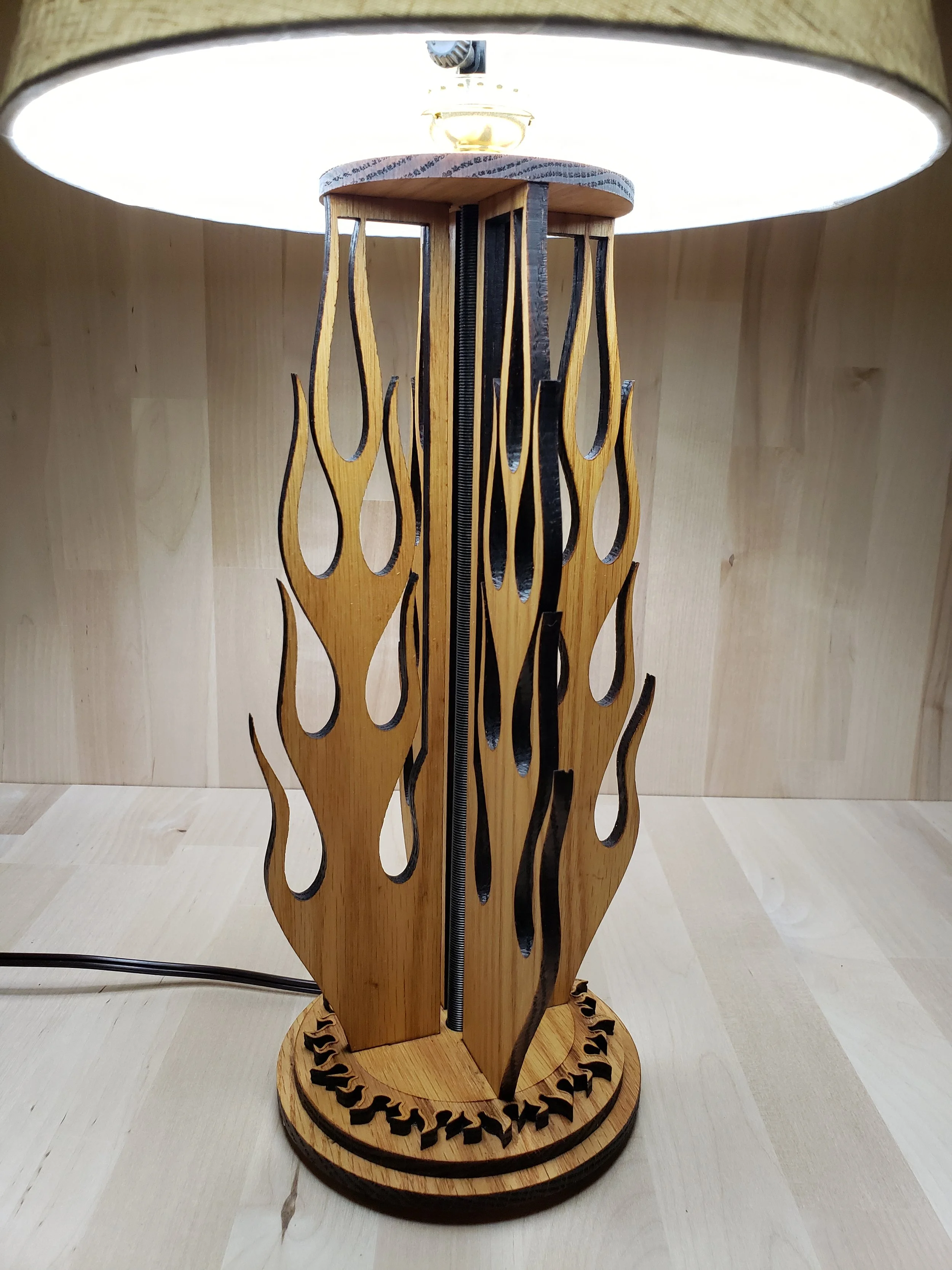 Wooden decorative sculpture with flame-shaped cutouts, mounted on a round base, illuminated from above.