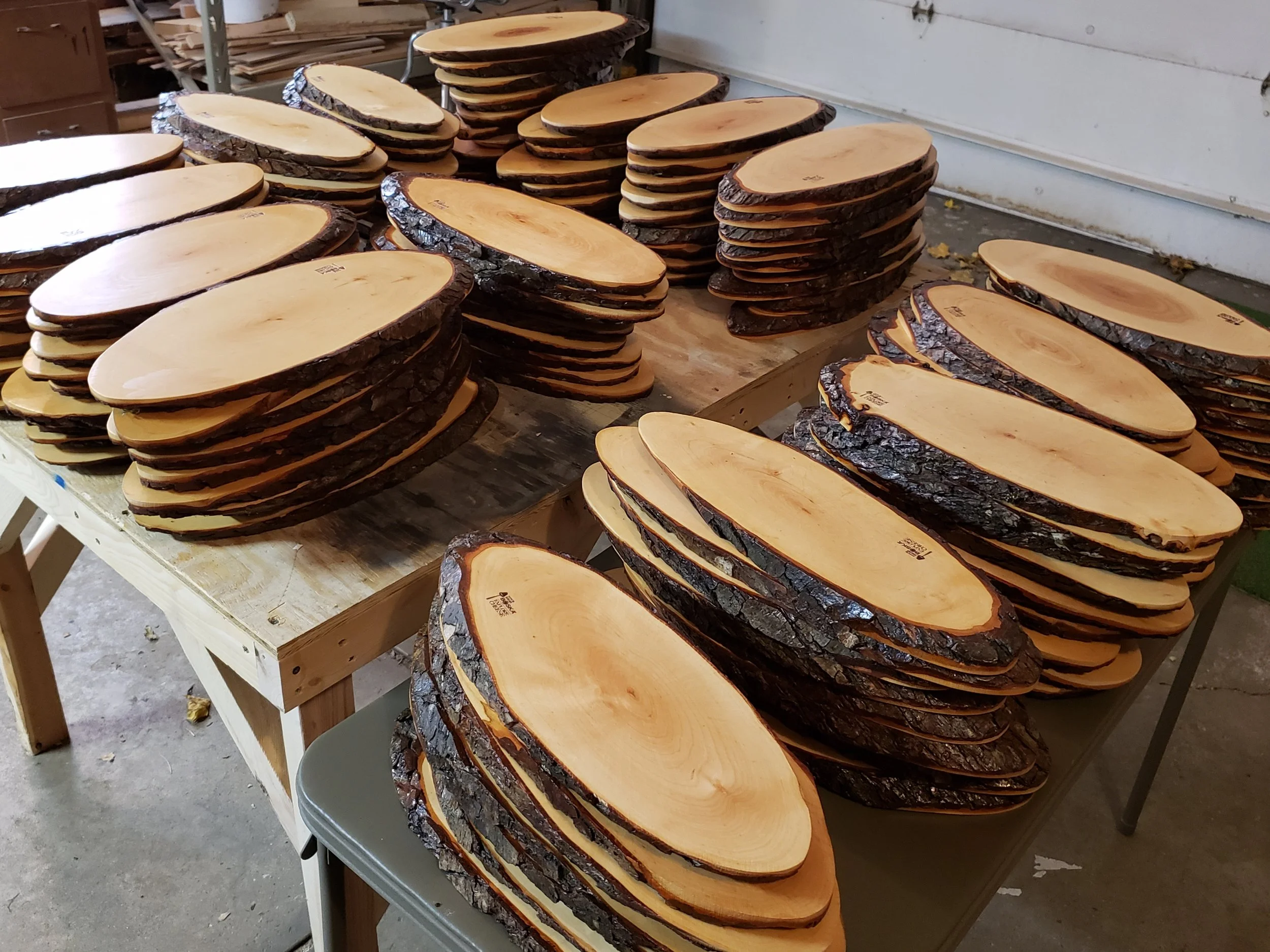 Stacks of wooden table slabs with bark edges, arranged on a work table in a workshop.
