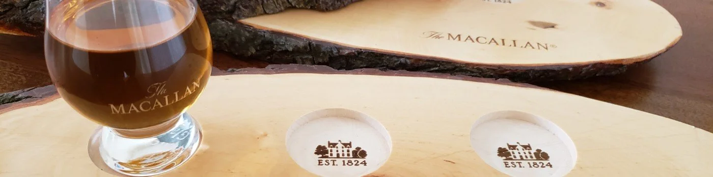 A glass of whiskey and two wooden coasters with the Macallan logo and 'EST. 1824' engraved on them.