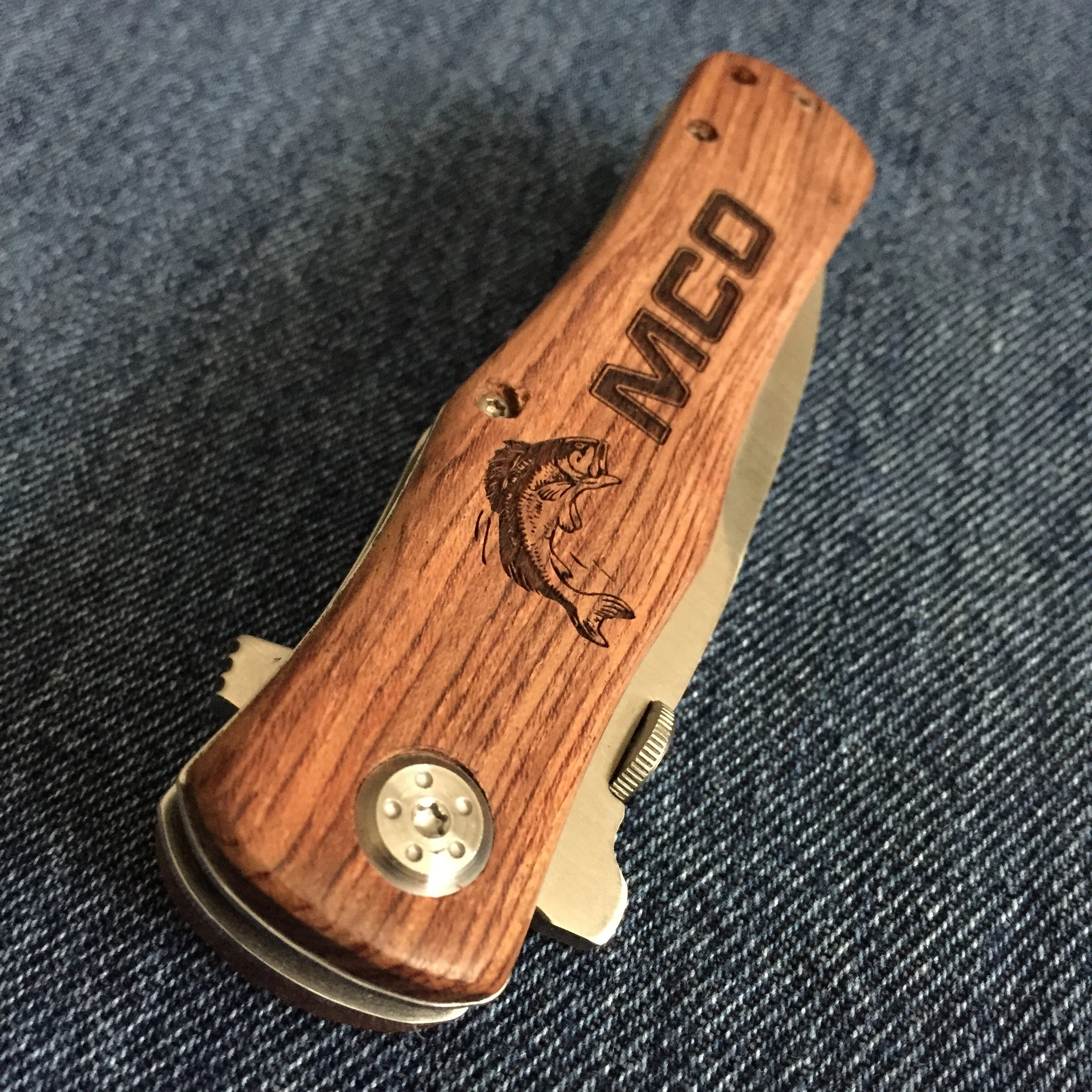 Close-up of a wooden knife handle with engraved text and a lion illustration, resting on dark fabric.