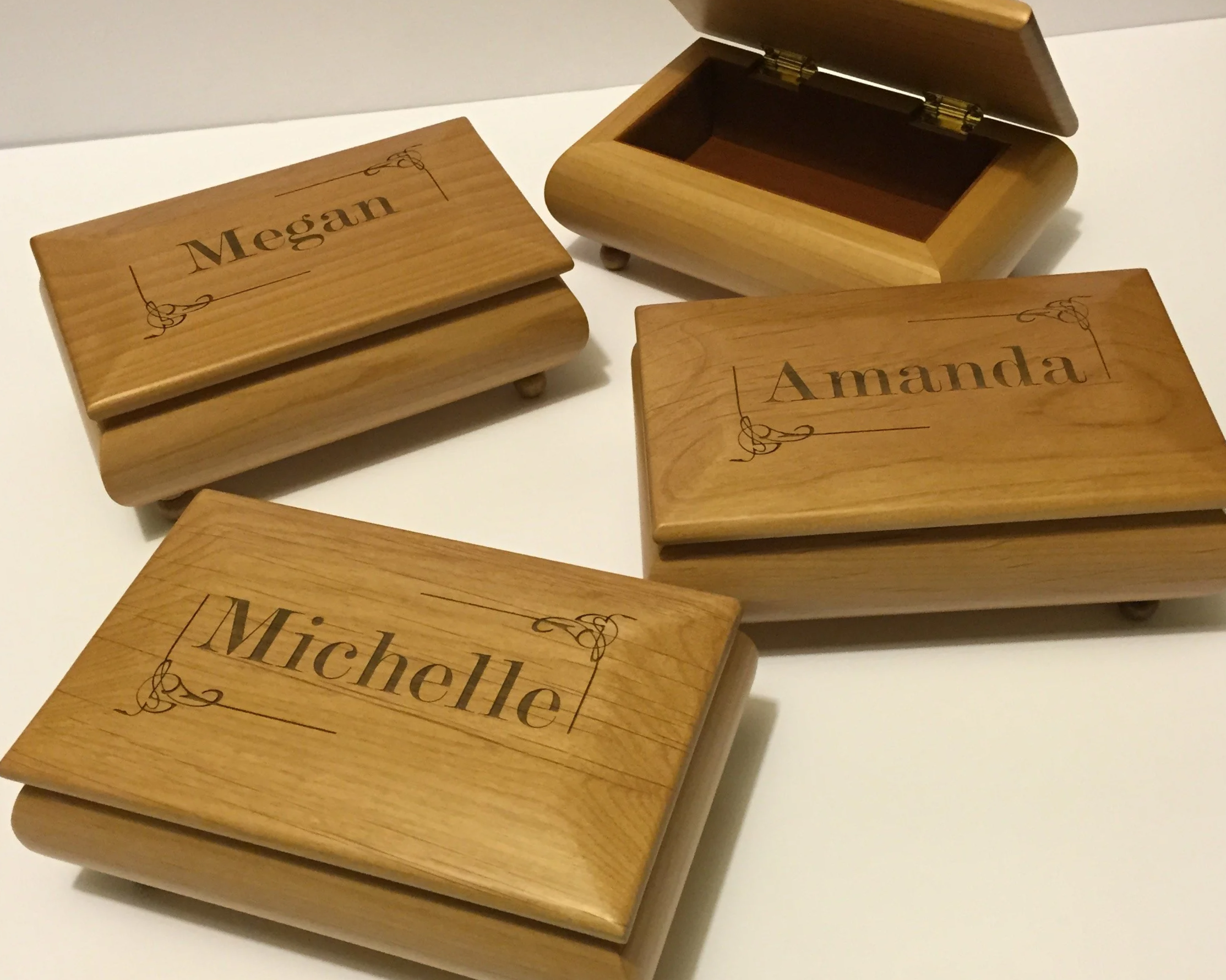 Three small wooden boxes with sliding lids, each engraved with a name 'Megan', 'Amanda', and 'Michelle', placed on a white surface.