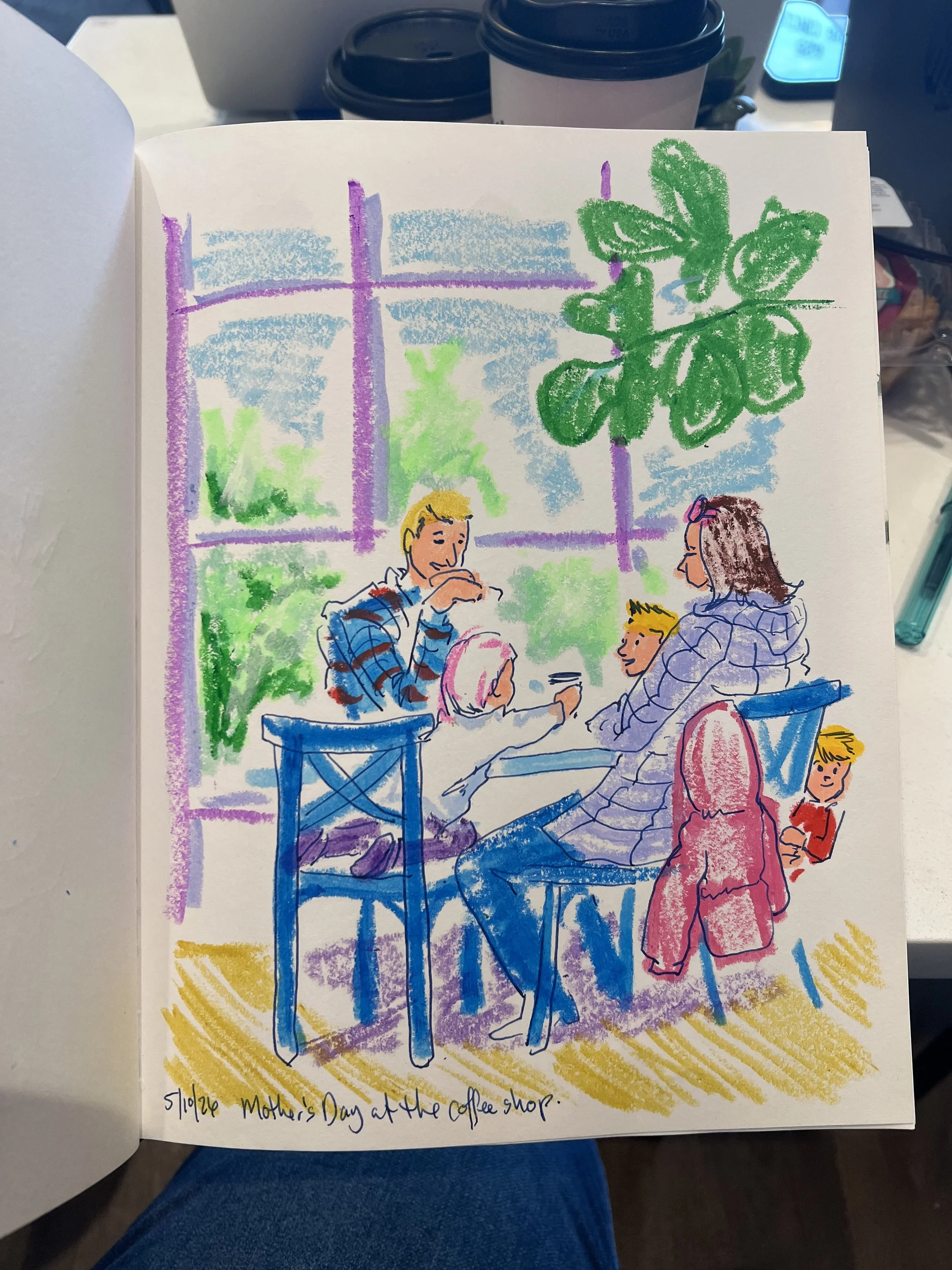A colorful drawing of a coffee shop scene with three people sitting at a table, a woman standing, large window with plants outside, and a handwritten note at the bottom reading "Mother's Day at the coffee shop."