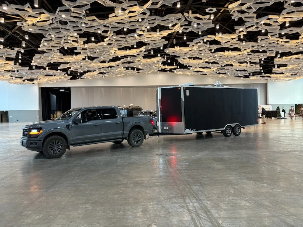 A dark gray pickup truck with a food trailer attached, parked inside the RBC Convention Centre, empty, modern indoor space with a decorative ceiling.