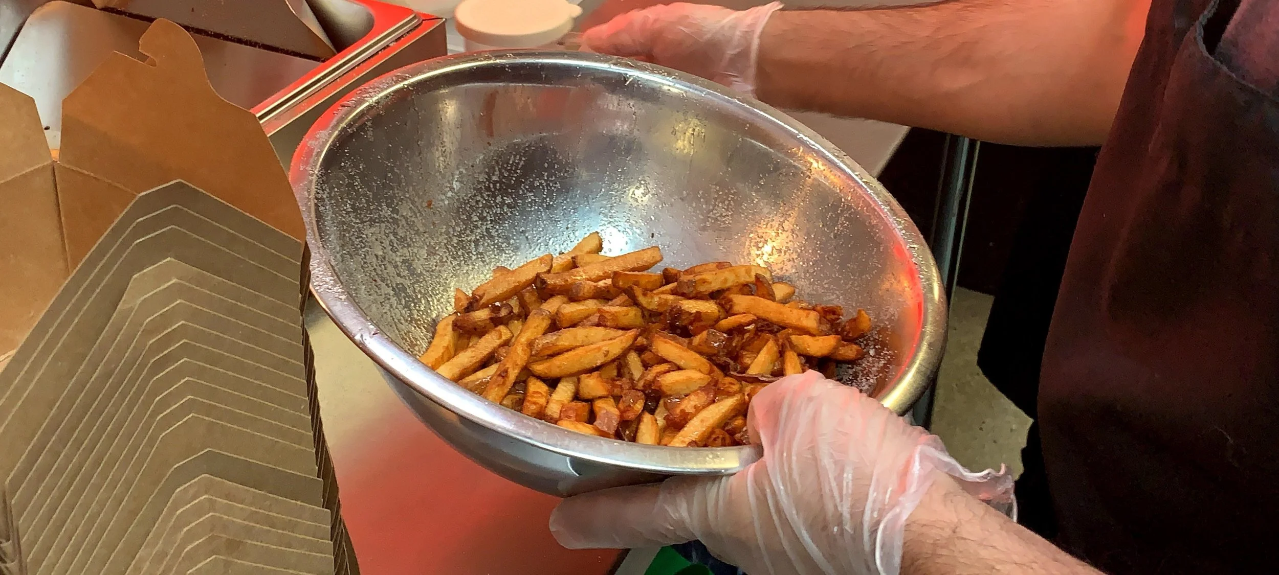 Person wearing gloves holding a bowl of cooked French fries.