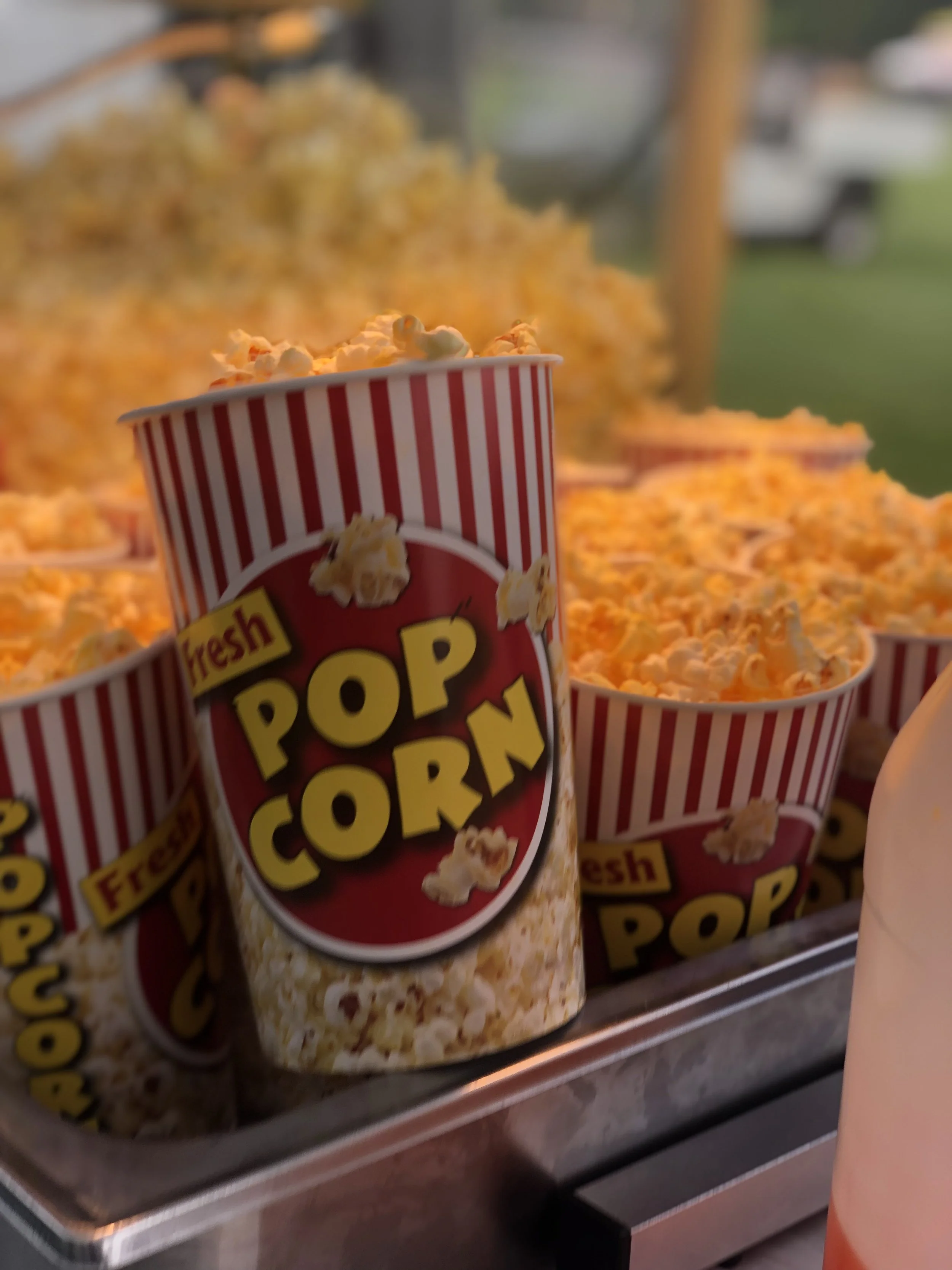Container of popcorn at a concession stand with more popcorn bags in the background.