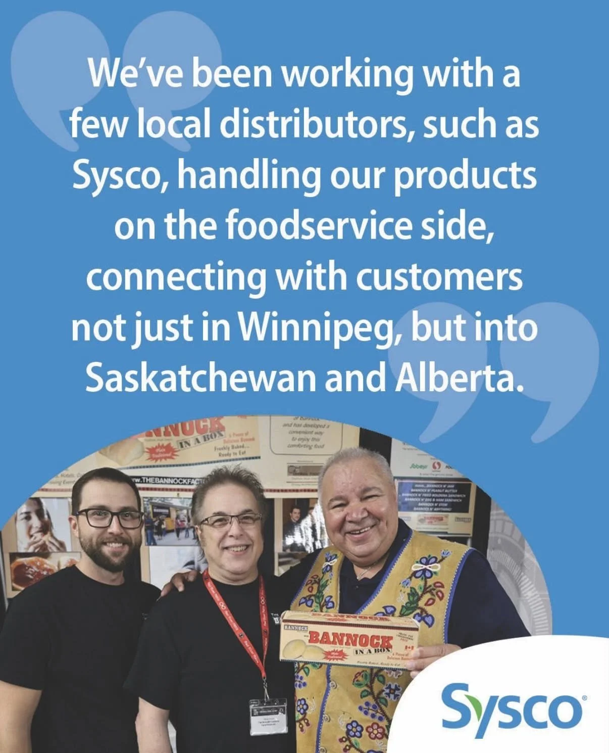 Three men smiling at the camera, one holding a box labeled 'Bannock In A Box'. They are standing in front of a booth with posters and signs, including Sysco branding.