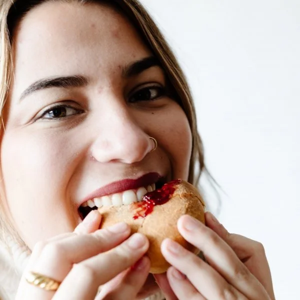A young woman with brown hair and a nose ring is about to bite into a warm piece of bannock, topped with strawberry jam
