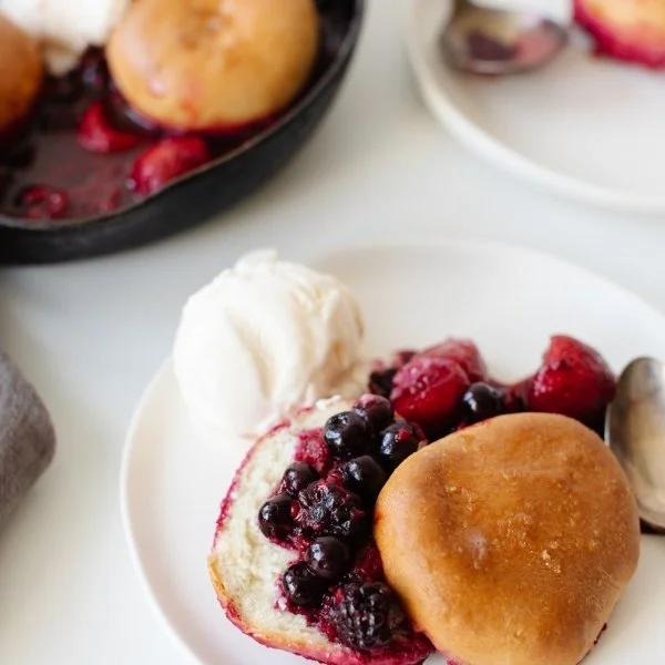 A white plate with a bannock buns, some mixed berries, and a scoop of vanilla ice cream.