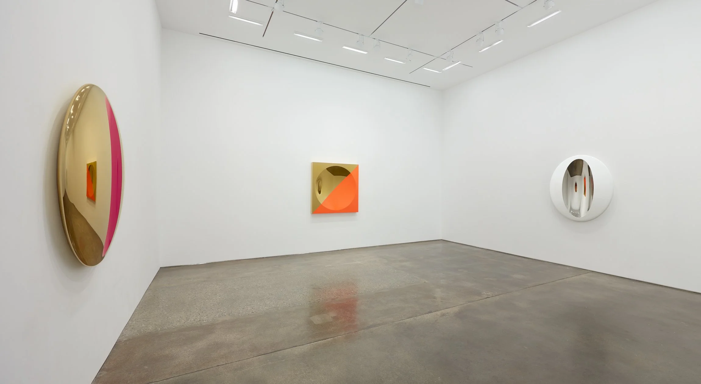An art gallery with three abstract paintings on white walls, illuminated by ceiling spotlights. The floor is polished concrete.