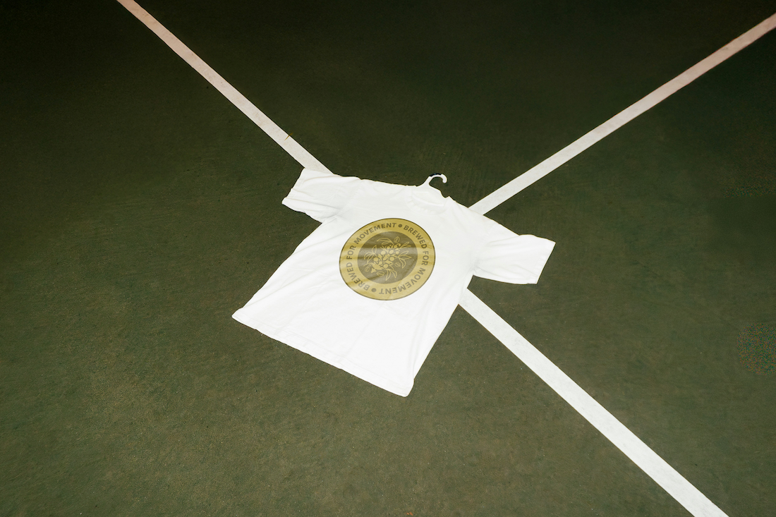 A white T-shirt with a round orange and gold logo placed on a green tennis court.