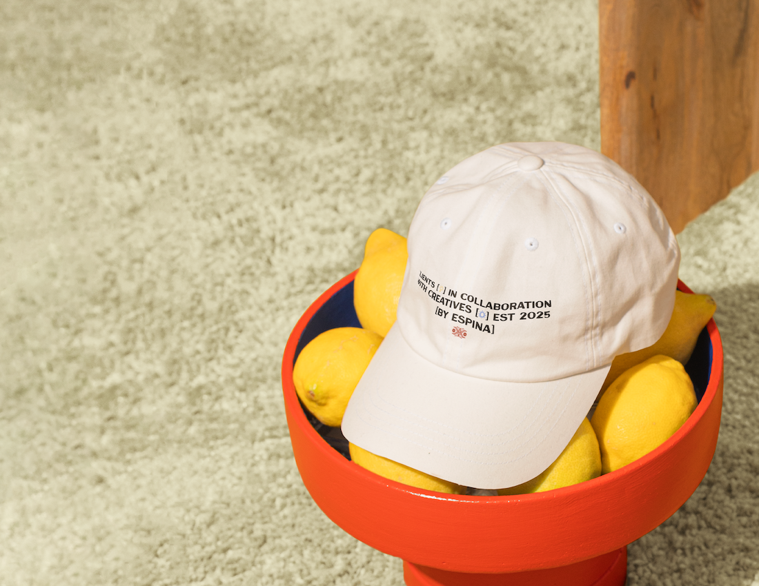 A red bowl filled with lemons with a white baseball cap placed on top of the lemons.