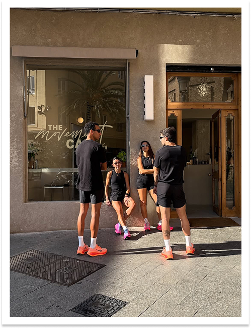 Four people dressed in athletic wear and sneakers are standing outside a building, engaging in a conversation.