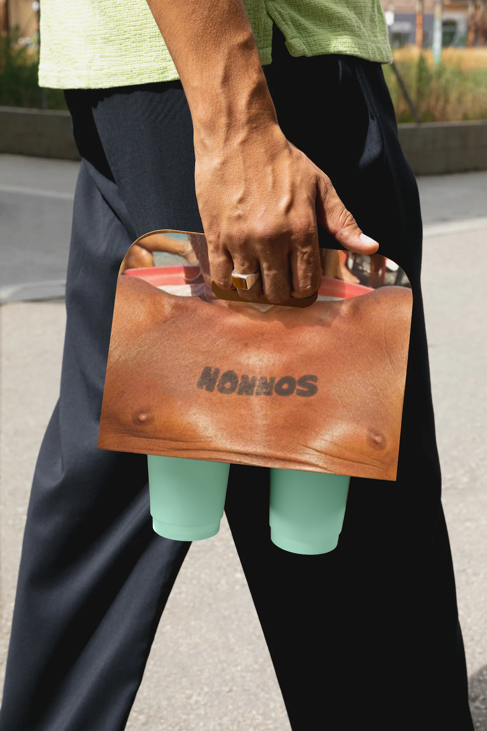 A person holding a paper bag with the word 'SOWON' printed upside down, containing two green cups. The person is wearing a light green shirt and black pants, standing outdoors.