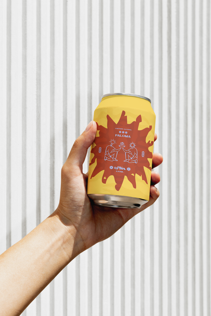 A hand holding a yellow can with a red and yellow label against a vertical metal siding background.