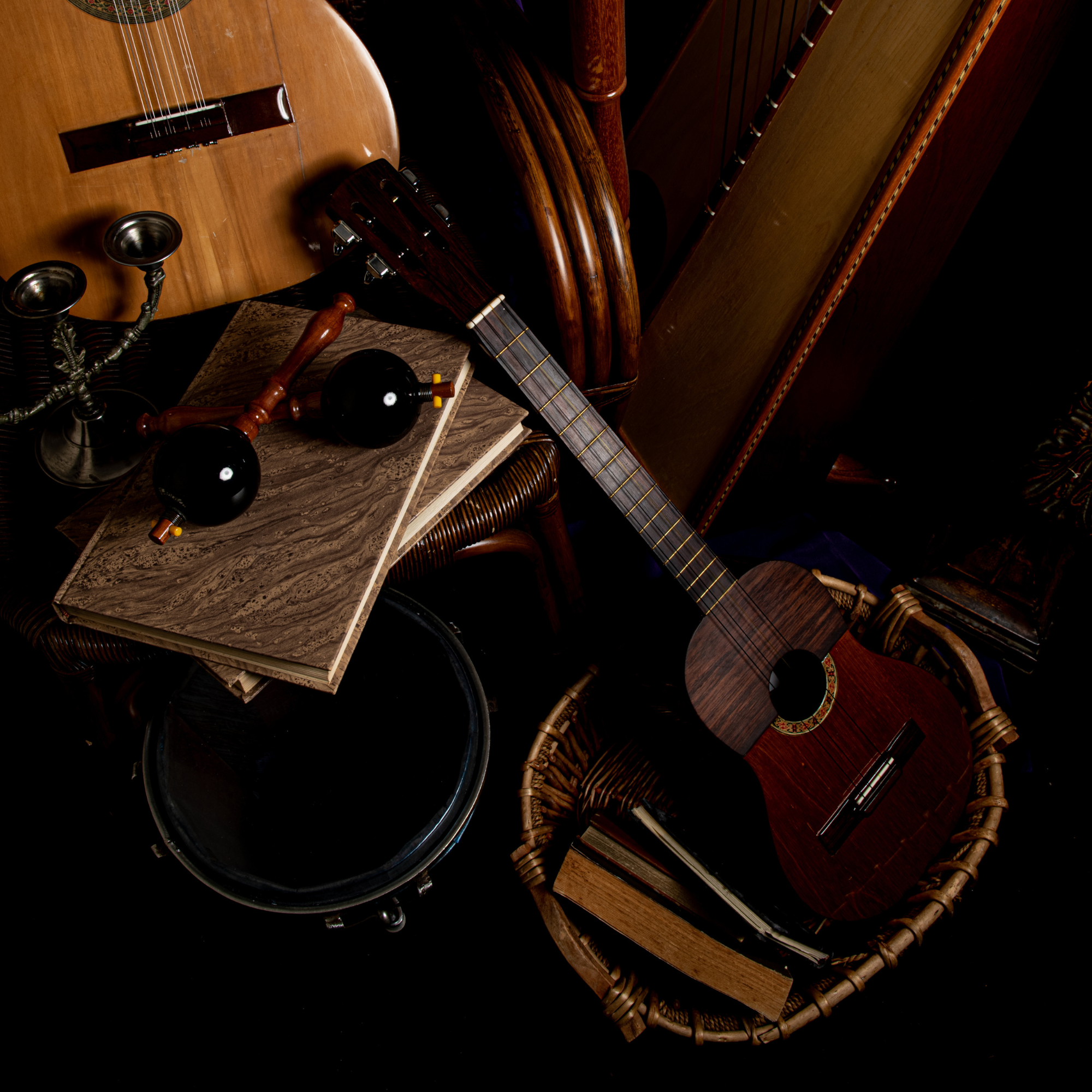 Close-up of musical instruments including a guitar, a balalaika, and a piano, with a vintage candlestick holder on a marble surface, and woven chairs around.