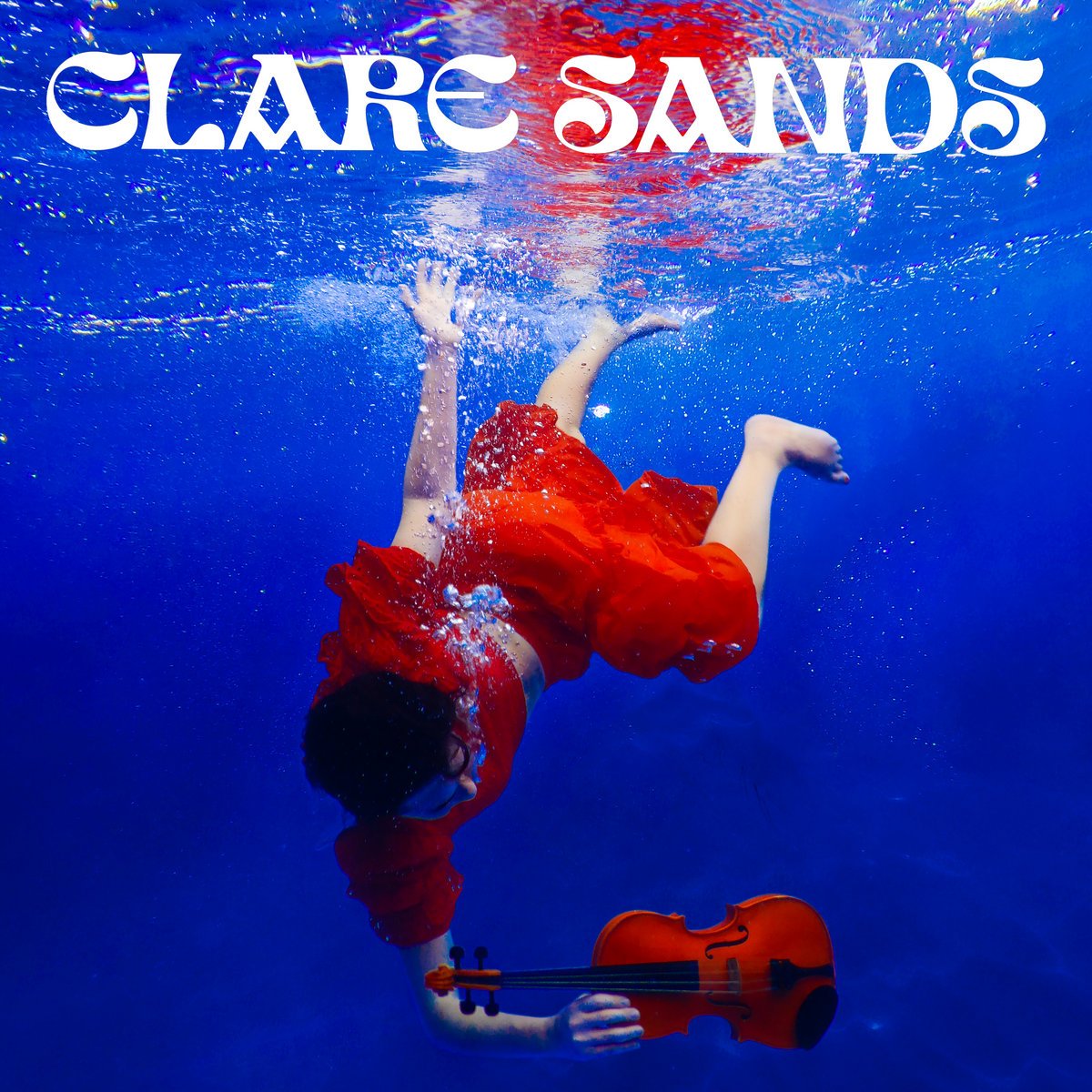 A person in a red dress submerged underwater holding a violin, with the text 'Claire Sands' at the top.
