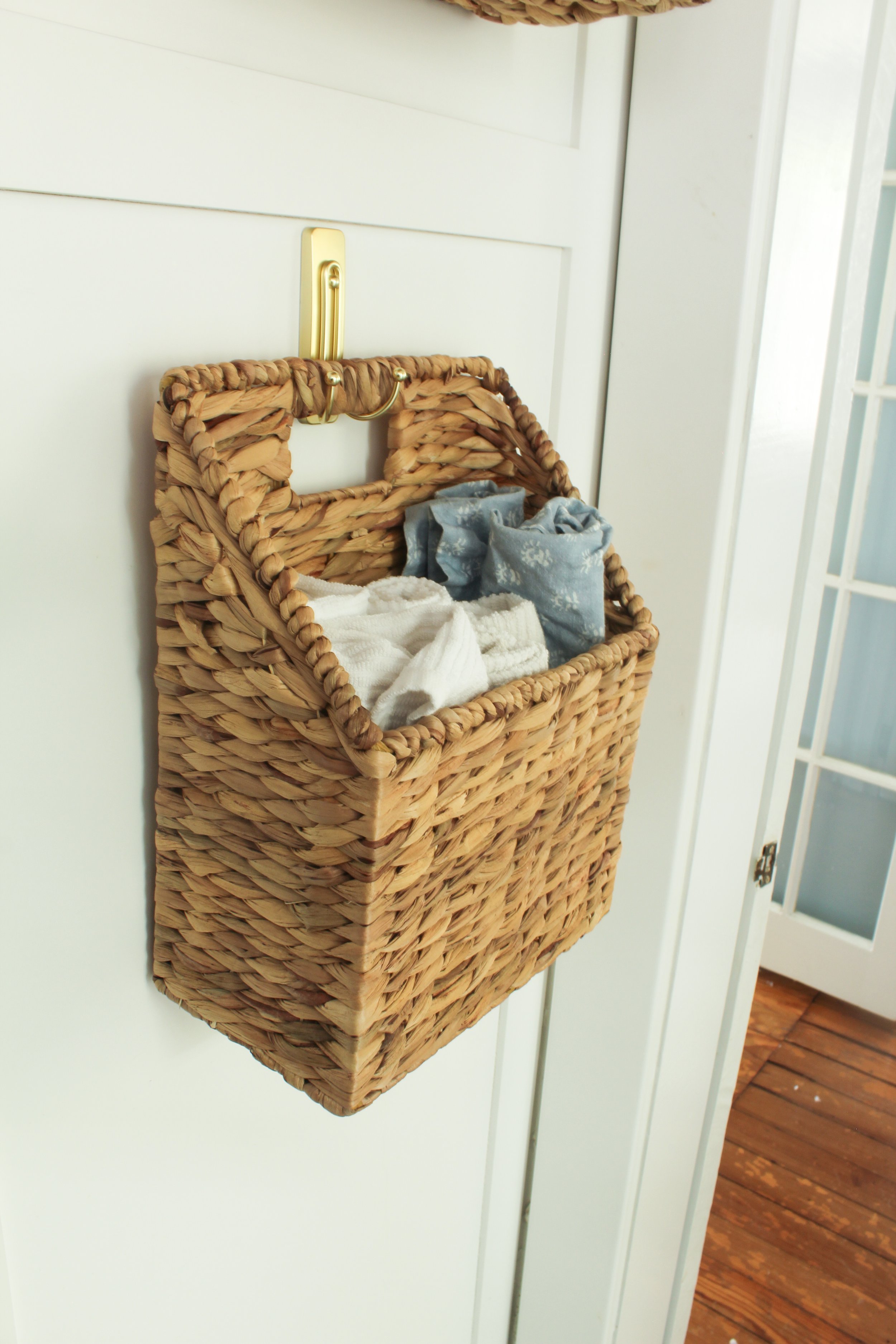 Wicker basket hanging on a white wall with clothes inside, next to a door with glass panels and wooden flooring.