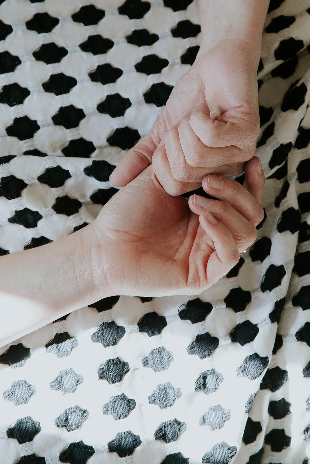 Two hands gently holding each other atop a black and white polka dot fabric background.