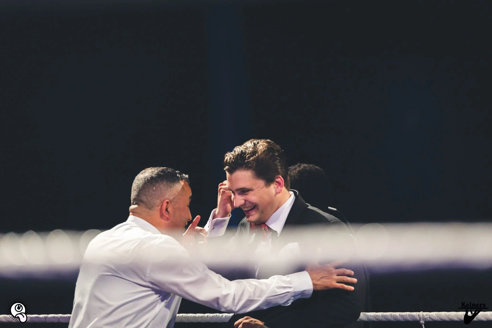 Twee mannen in een ring, lachend en met vriendelijk gebaren, die een emotioneel moment van vreugde of felicitatie delen