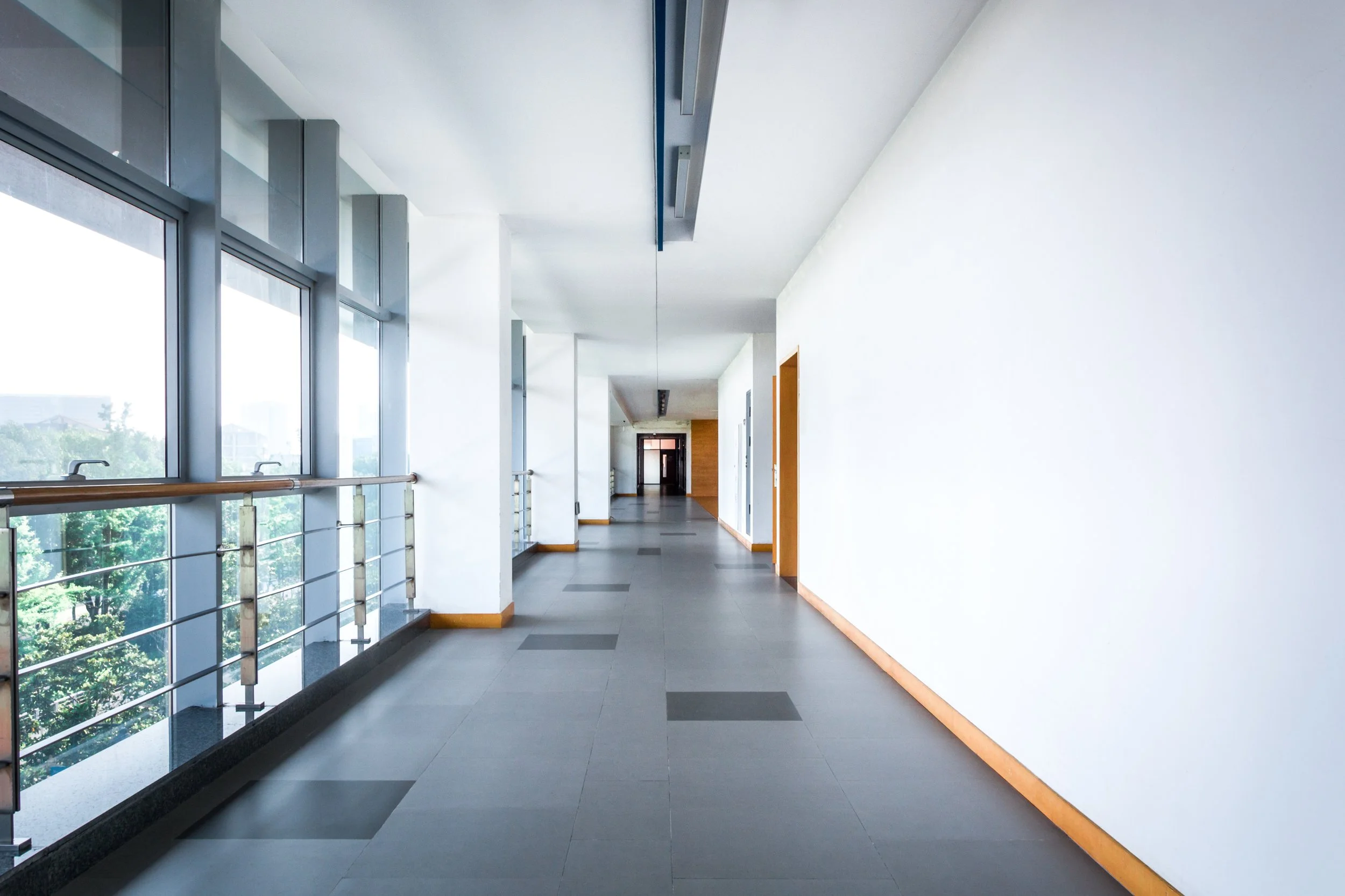 Freshly painted white walls in a modern commercial building hallway with large floor-to-ceiling windows and gray tile flooring
