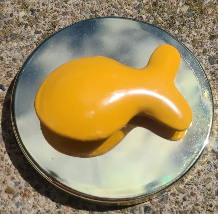 A yellow, dog-shaped object on a round mirror placed on a textured surface.