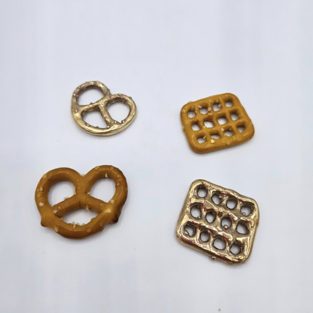 Four small pretzel-shaped and waffle-shaped metallic and plastic items on a white surface.