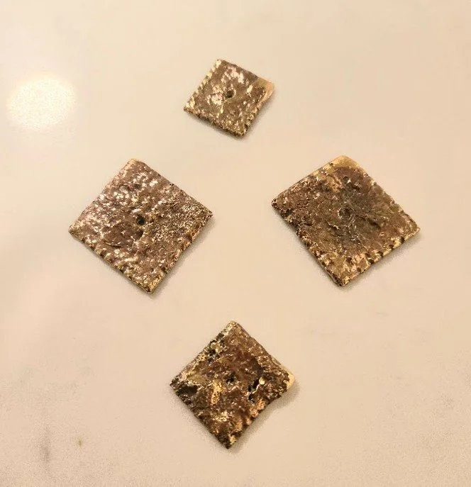 Four small, rusty metal squares arranged in a diamond pattern on a plain, light-colored surface.