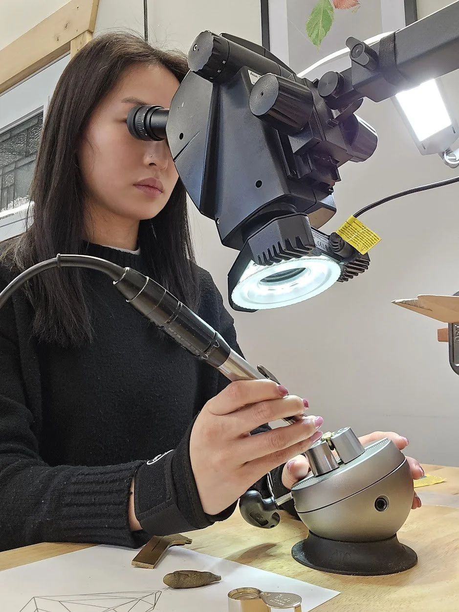 A woman using a microscope in at a stone setting bench with ball vise. A women setting stones using flex shaft micromotor and ball vice and microscope.
