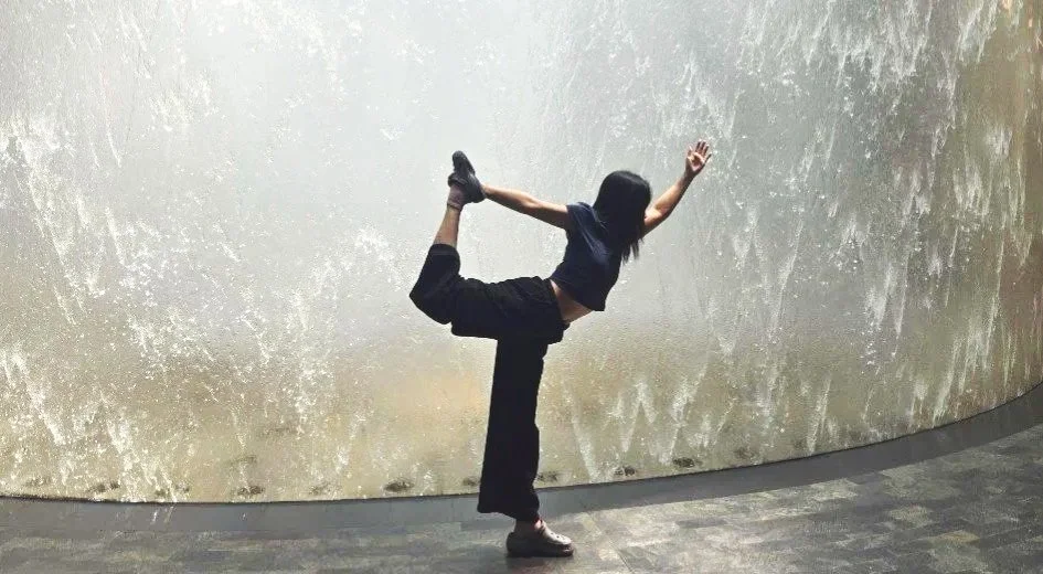 Person performing a dance or yoga pose in front of a textured, metallic wall.