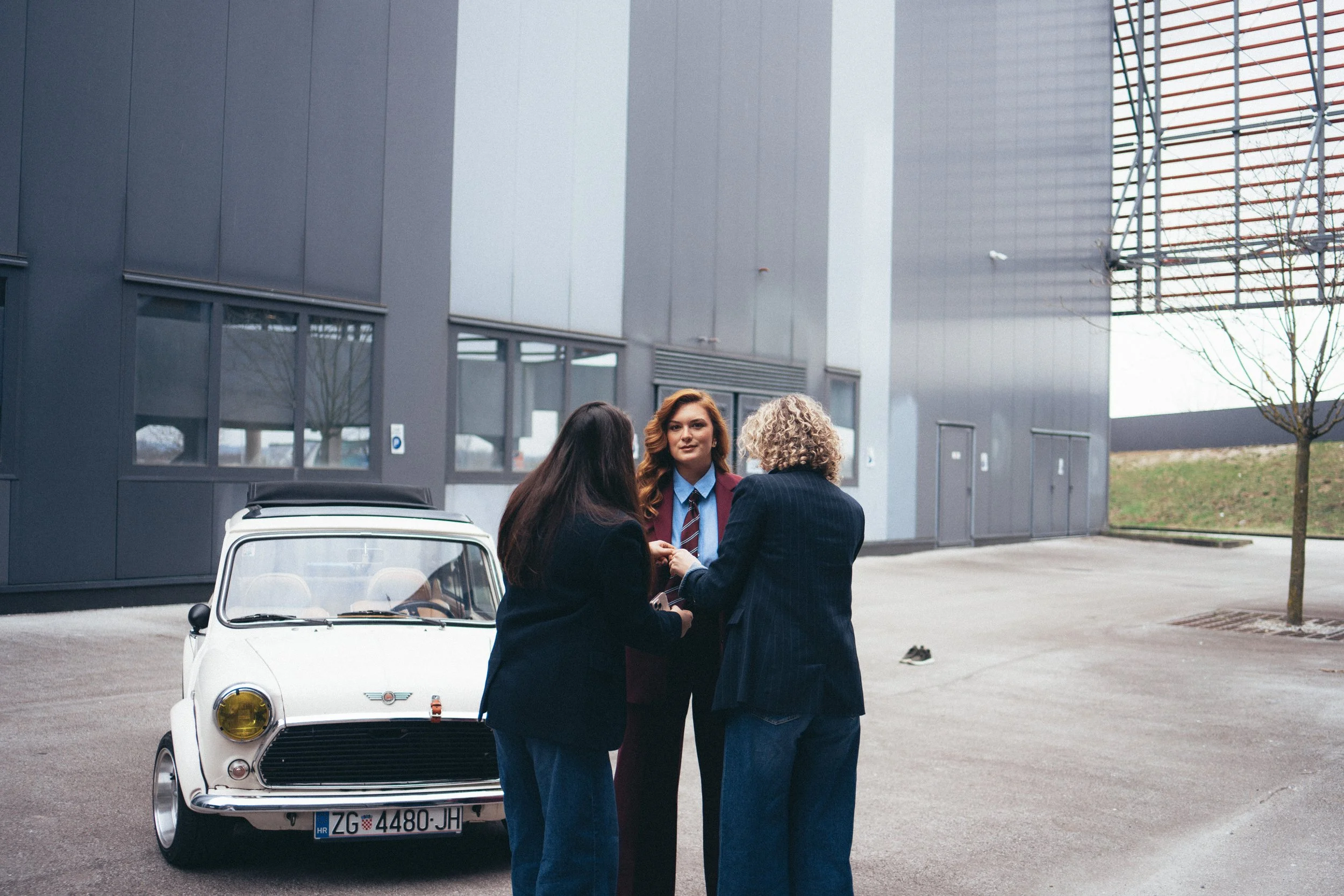 Behind the scenes of with personal stylists assisting on a personal branding photoshoot. They are dressed in professional or business casual attire. The scene is set in an urban area with modern buildings and scaffolding visible in the background.